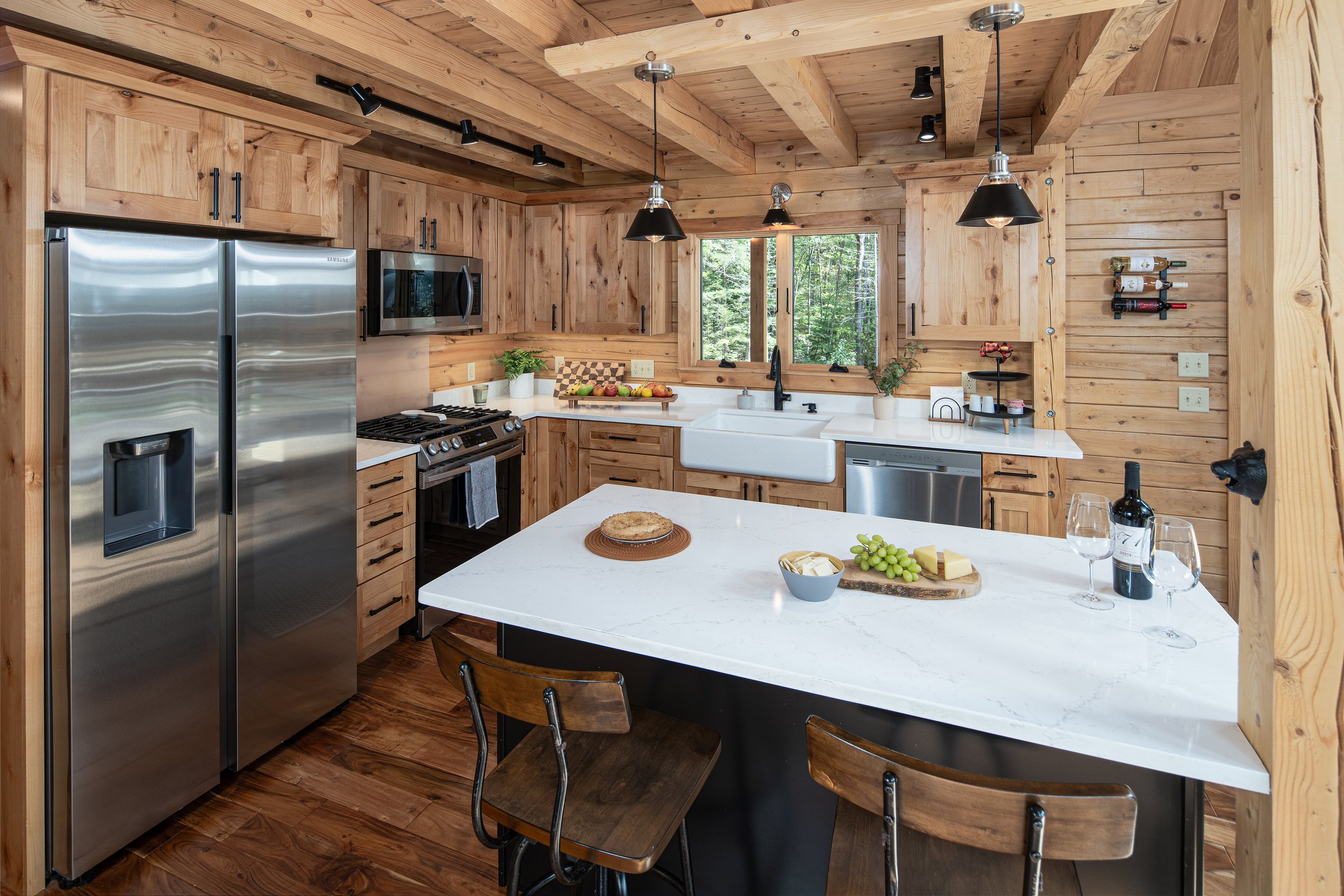 The white stone countertop adds a contemporary touch, balanced with rustic elements like sturdy black cabinet hardware and a timeless farmhouse sink. Understated pendant lights add functionality without overwhelming the design.