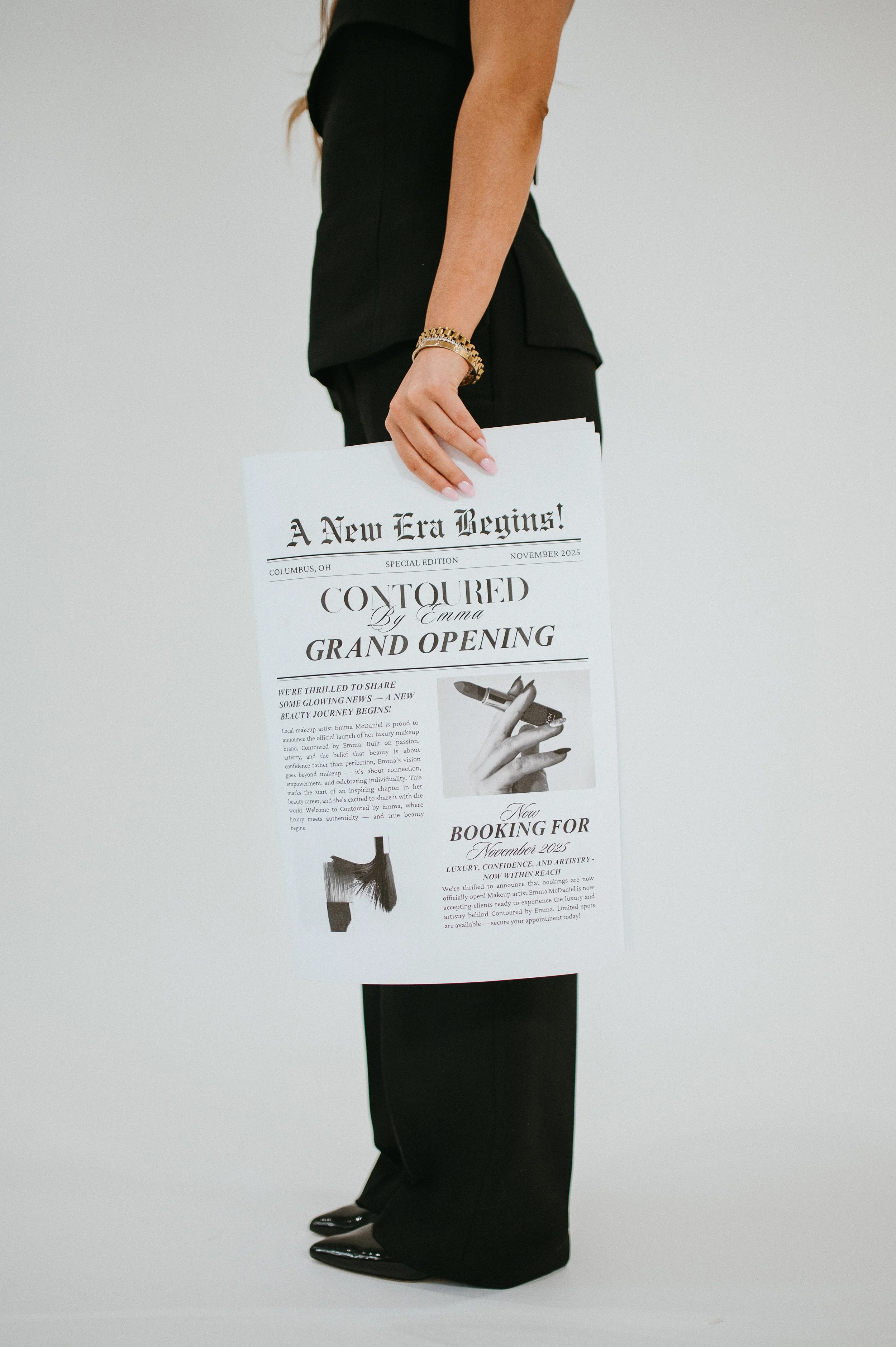 Branding photo of a woman in black clothing and shiny black shoes holding a flyer for a grand opening event in Columbus, Ohio, titled 'A New Era Begins' with articles and images related to beauty and makeup.