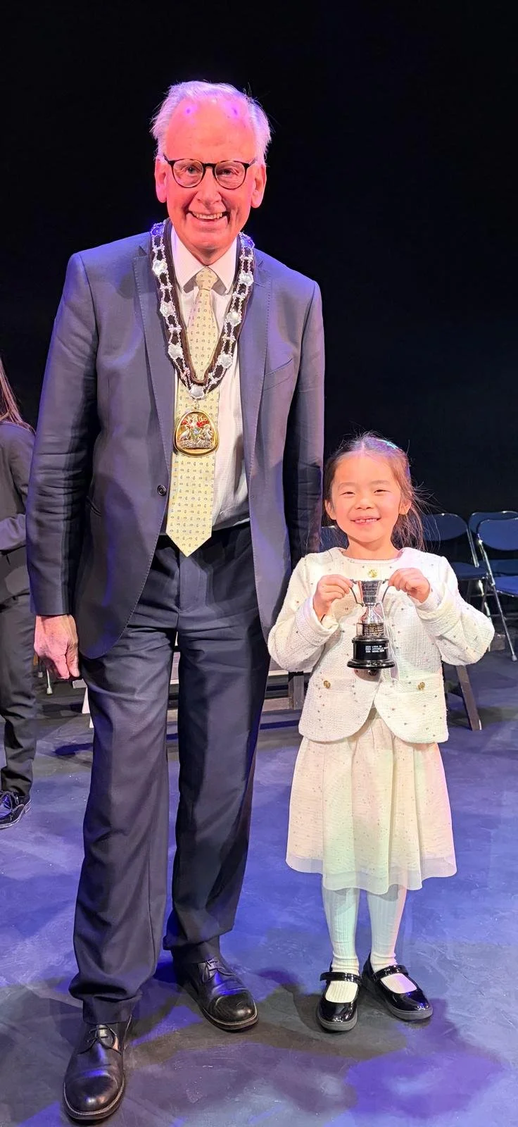 7 year old Nabit stands on stage at Gems concert beside the major in adorned with his chain of office.