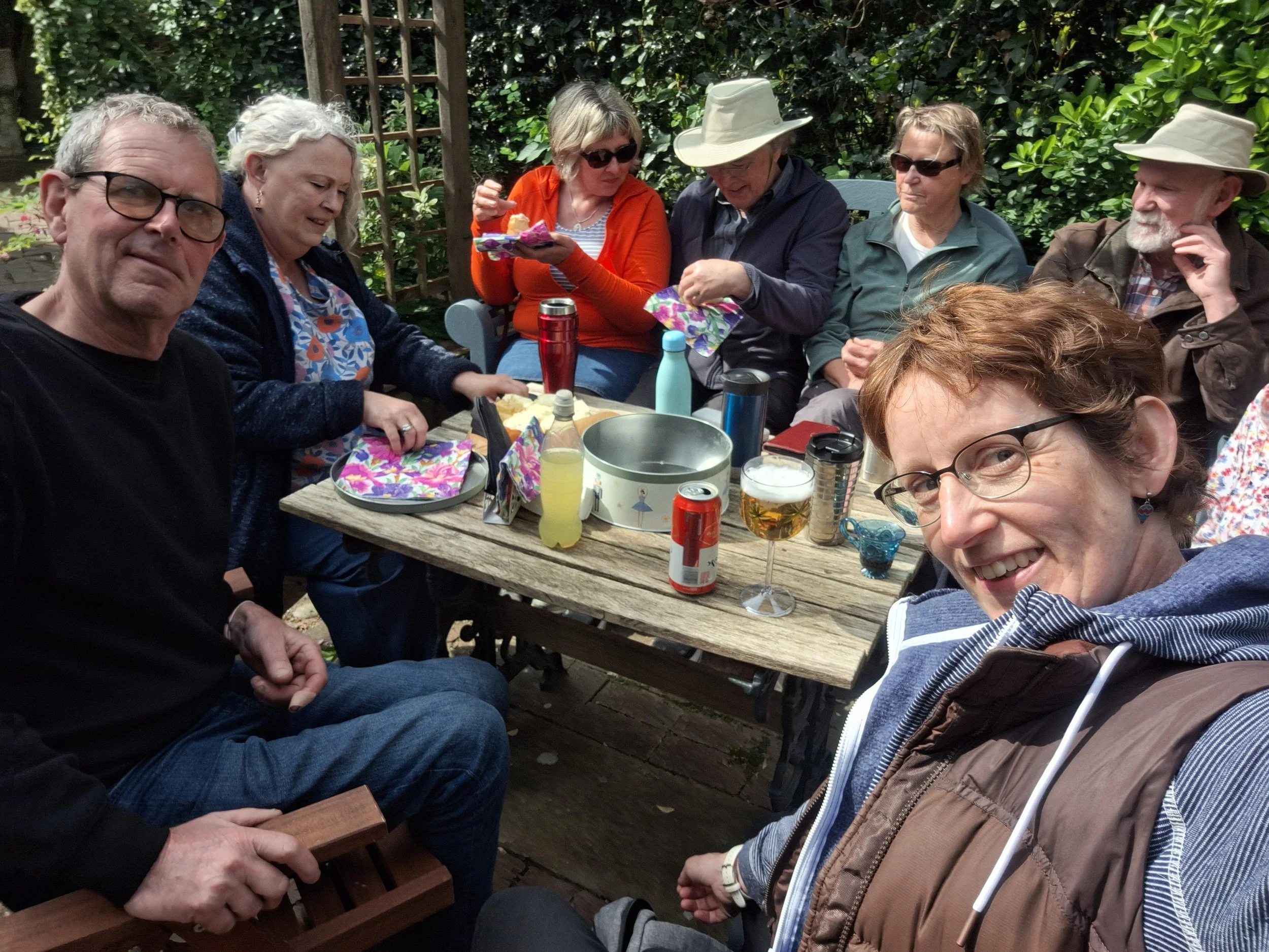 Group of mixed aged adult socialising in garden party with cake.  It's summer and they are smiling.