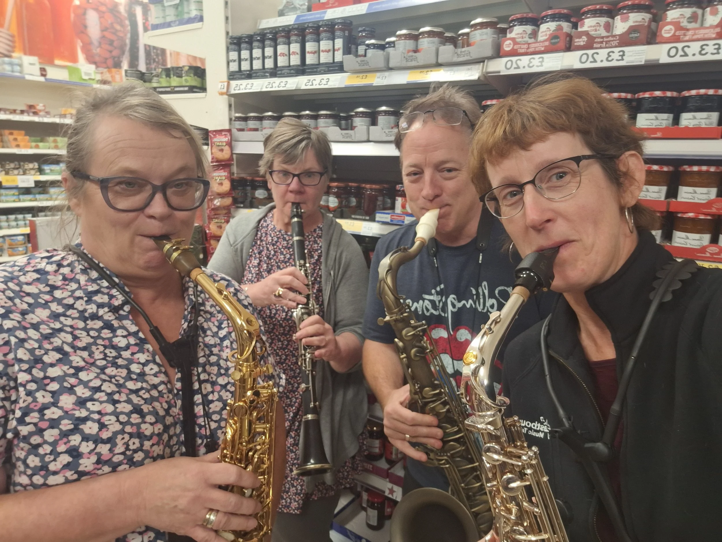 3 ladies and 1 man stand in the jam isle of Teso pretending to play.  Two hold alto sax, one tenor and one clarinet, they are holding back laughs with a new joke jamming in the jam isle.
