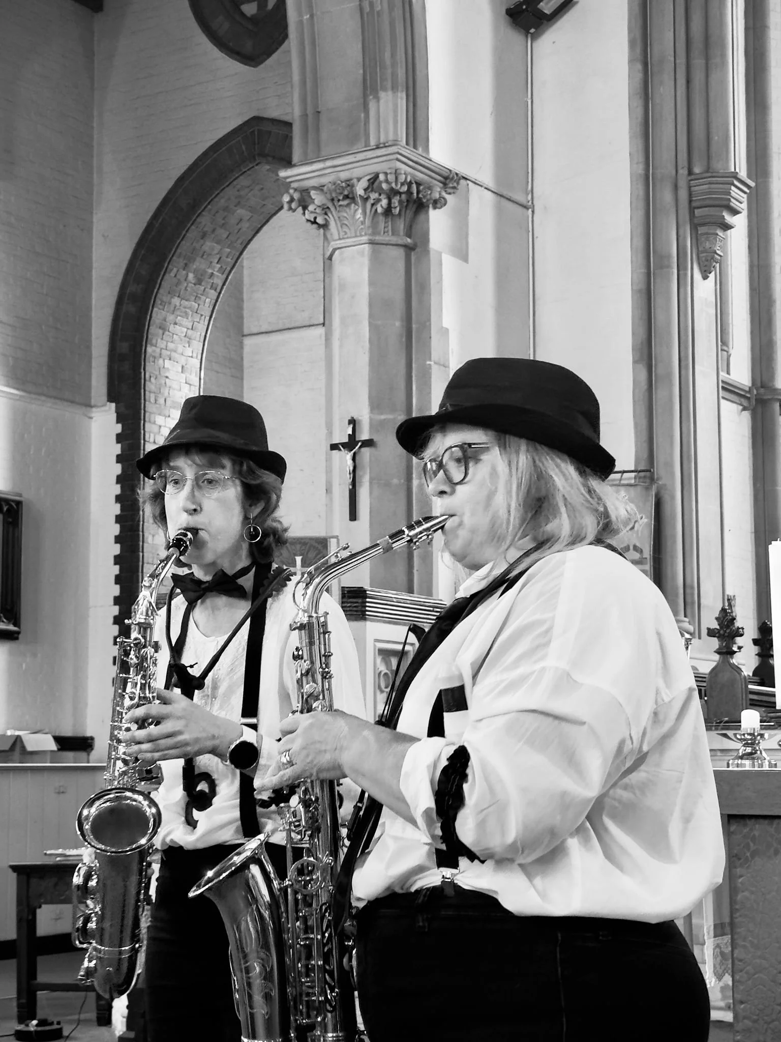 2 middle aged ladies dressed as blues brother play alto sax in a church setting.