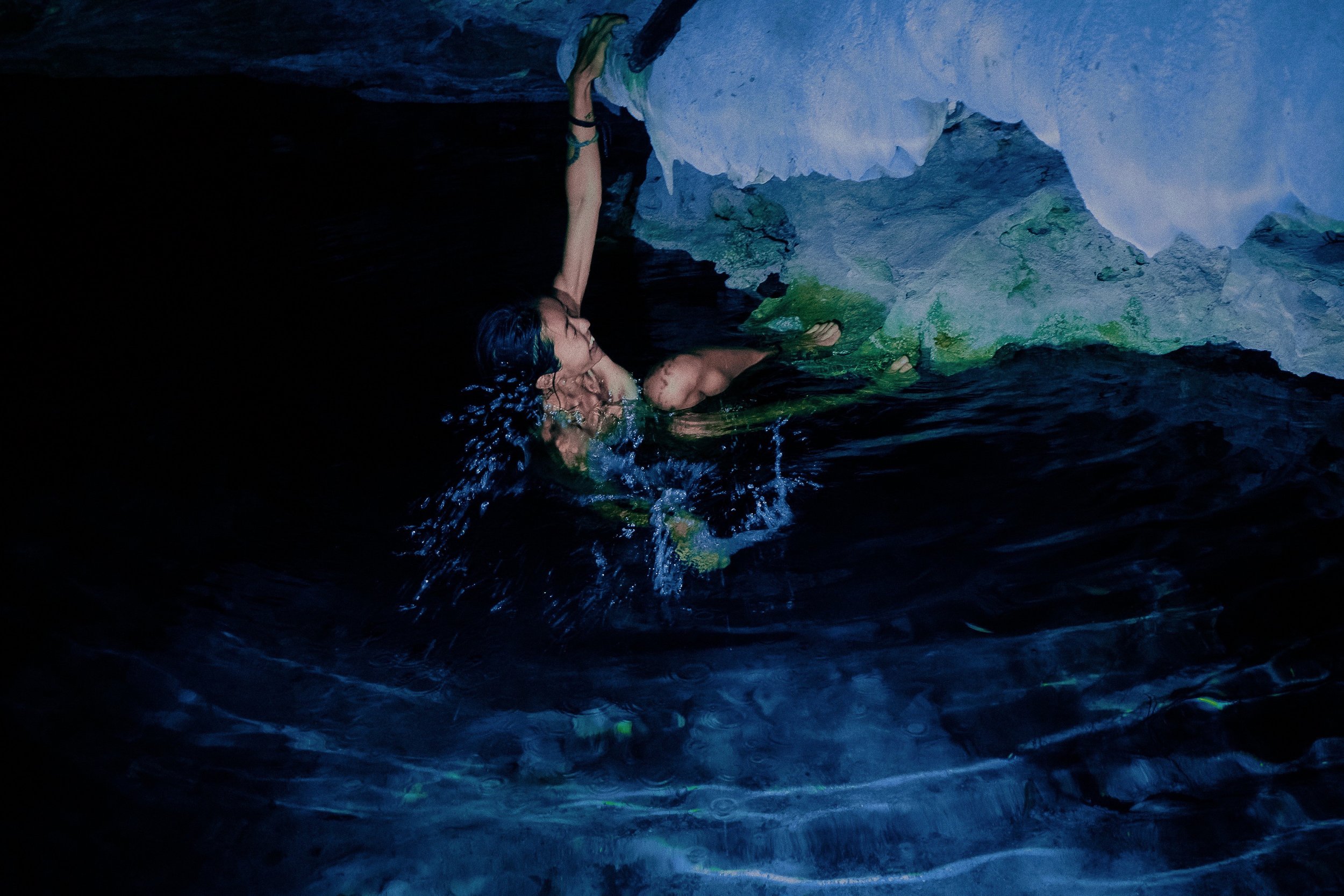 Person rock climbing in a dark, aquatic cave environment.