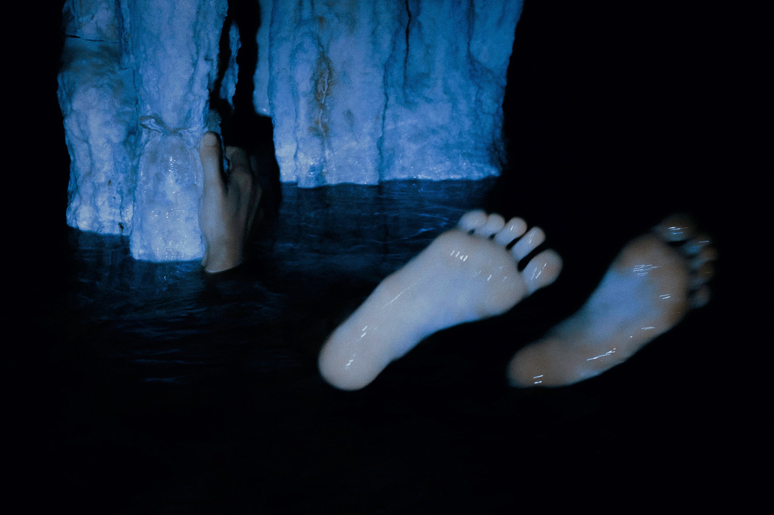 Feet and a hand in water near illuminated cave walls.
