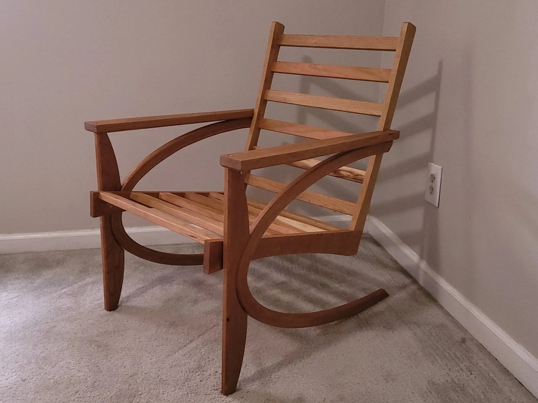 Wooden rocking chair placed on beige carpet with a plain wall background.