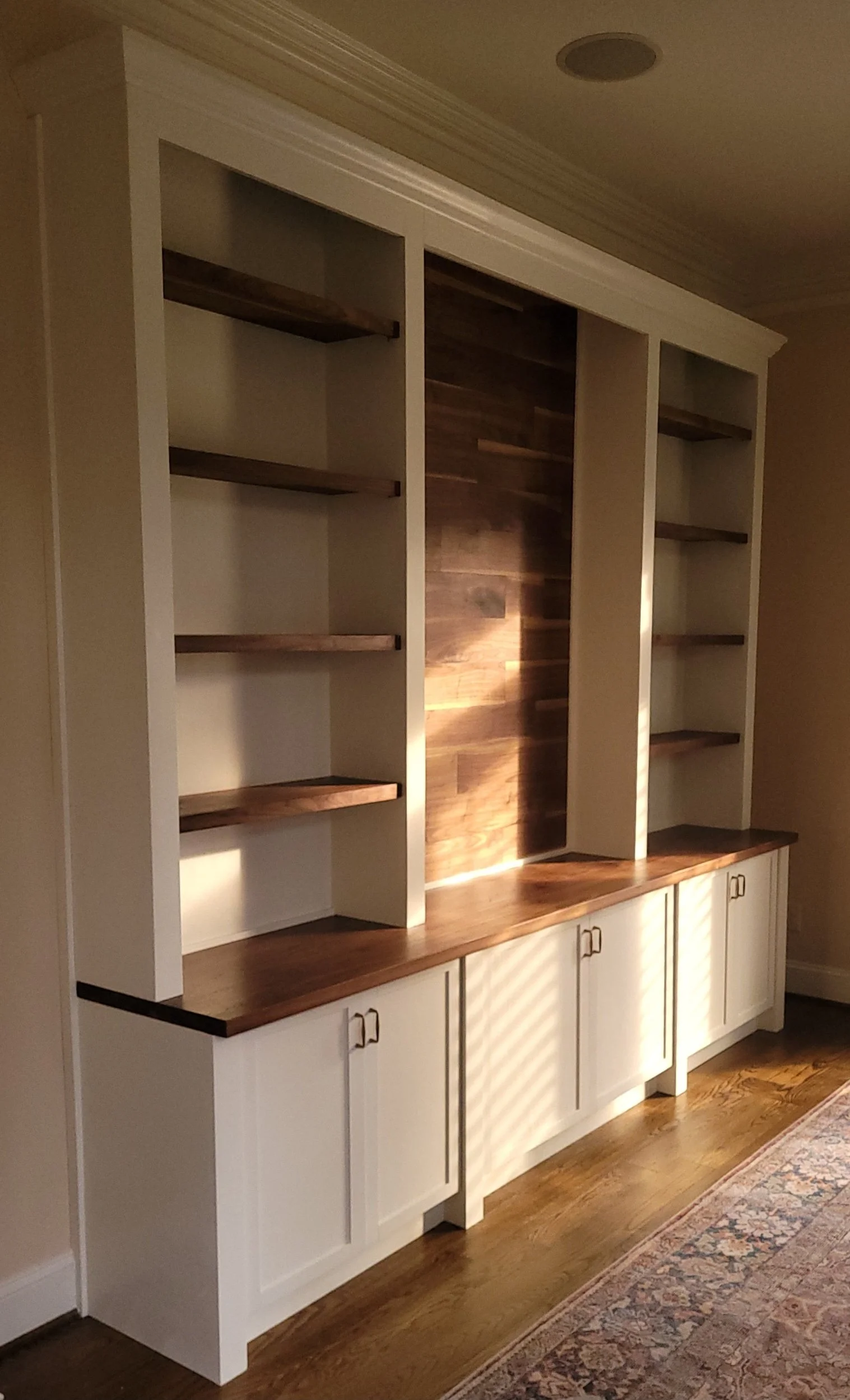 Built-in white cabinetry with open shelves and a wooden countertop, set against a wall with a wooden accent panel and a ceiling with crown molding.