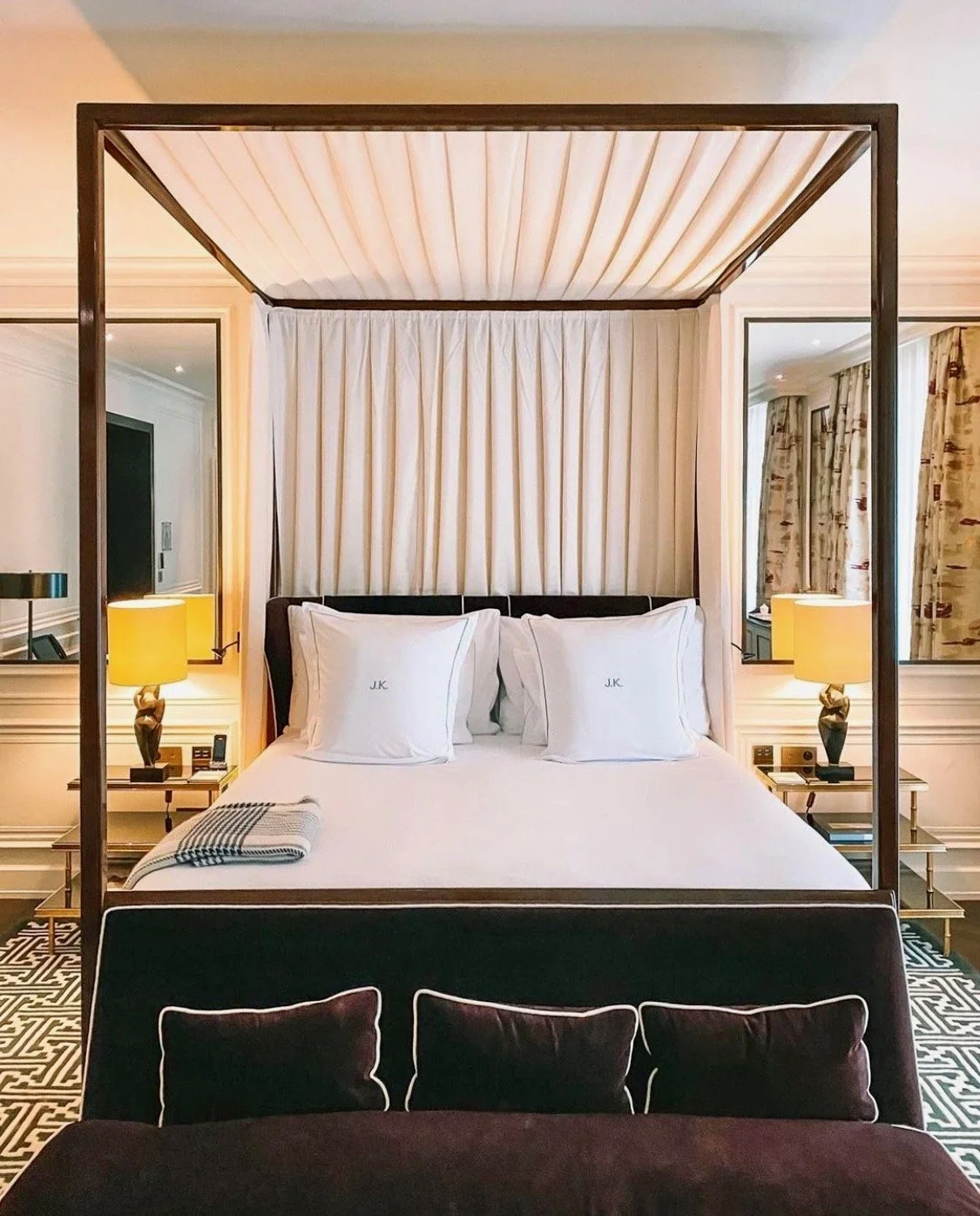 Elegant bedroom with four-poster bed, white canopy and pillows, bedside lamps, and patterned carpet.