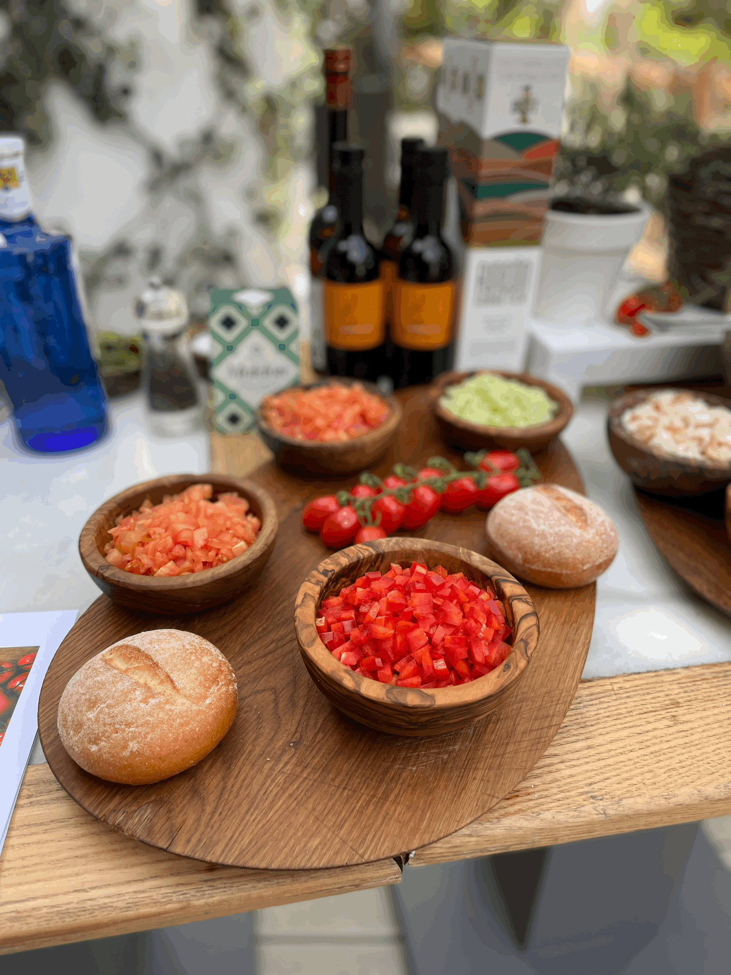 Ingredients for bruschetta preparation with diced tomatoes, peppers, onions, and bread on a wooden board, surrounded by olive oil bottles.