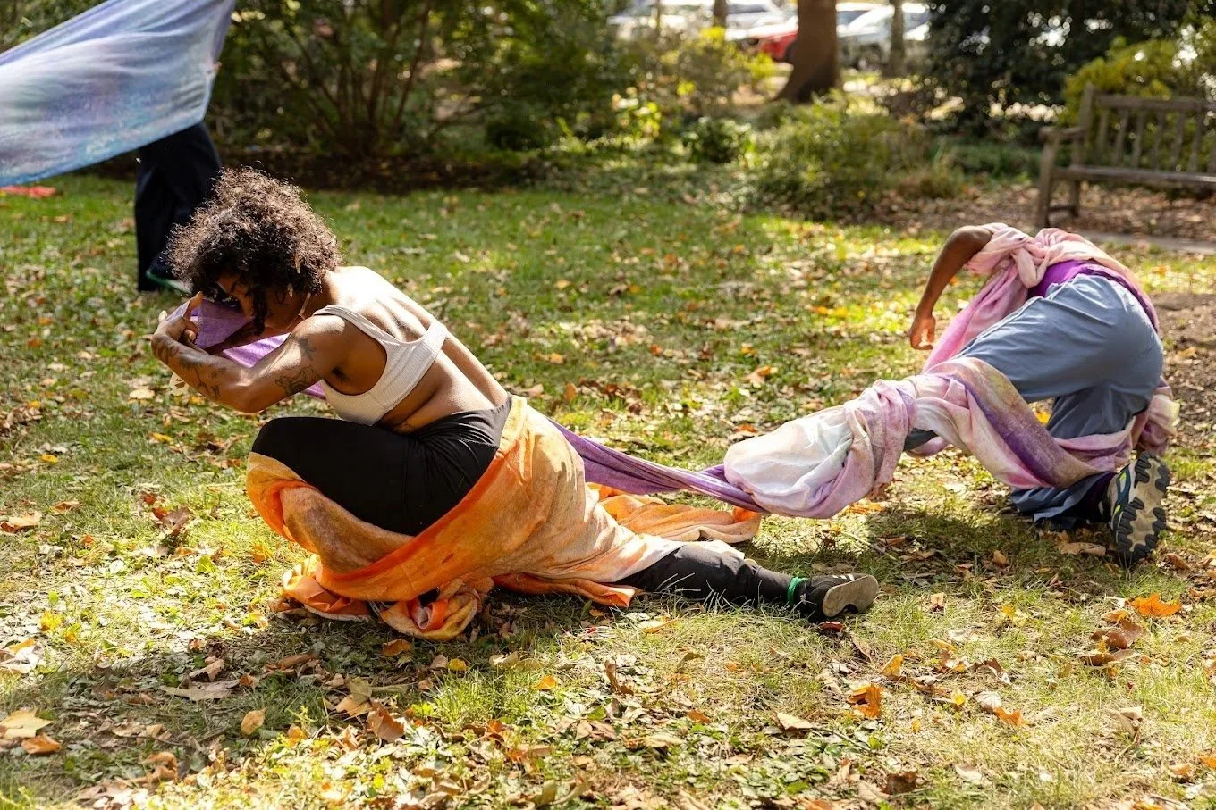 Two dancers draped in colorful scarves pull away from each other as part of a performance piece.