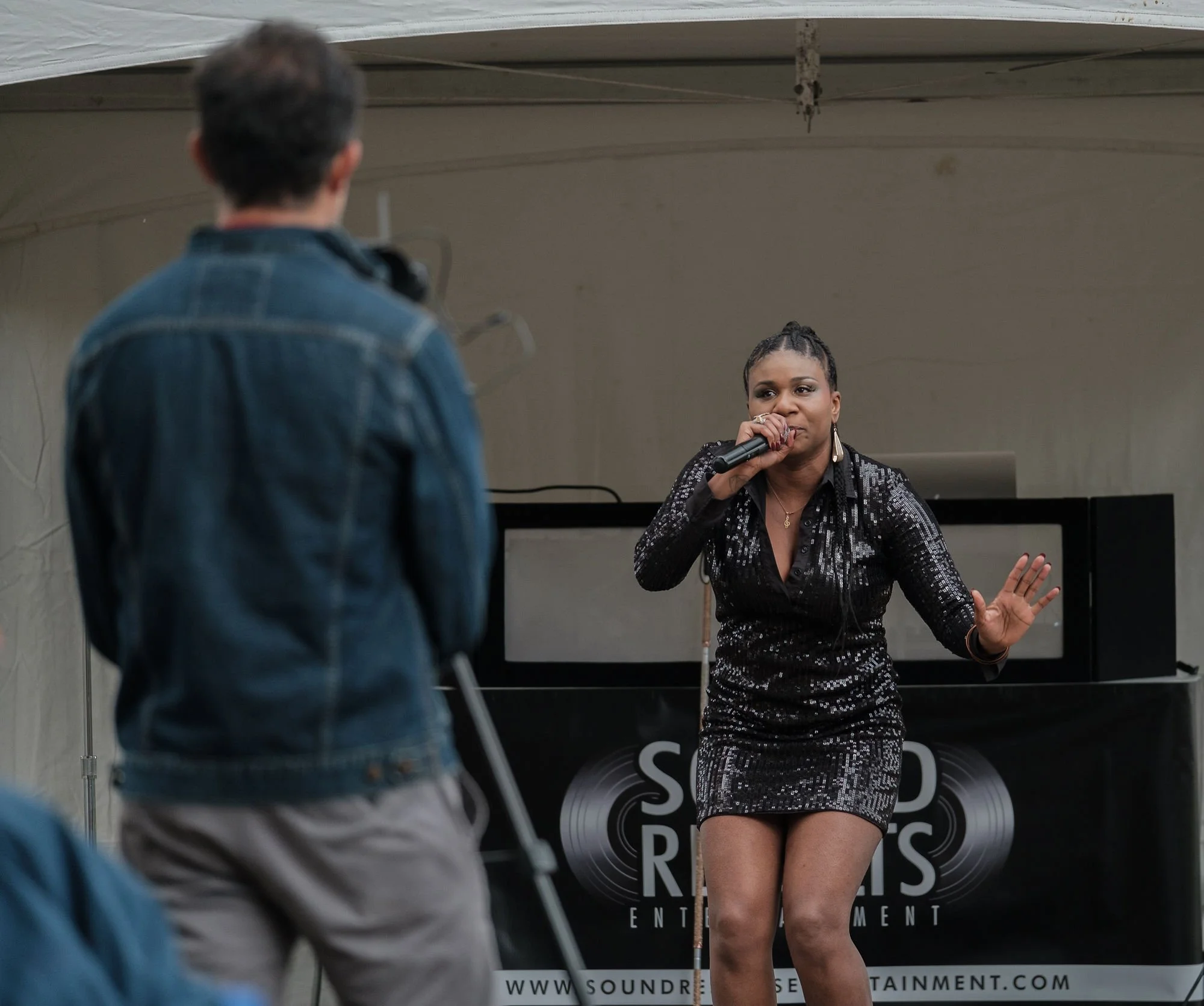 Lachi performing in black sequin dress at Disability Pride Central PA with the back of Maynor filming the performance