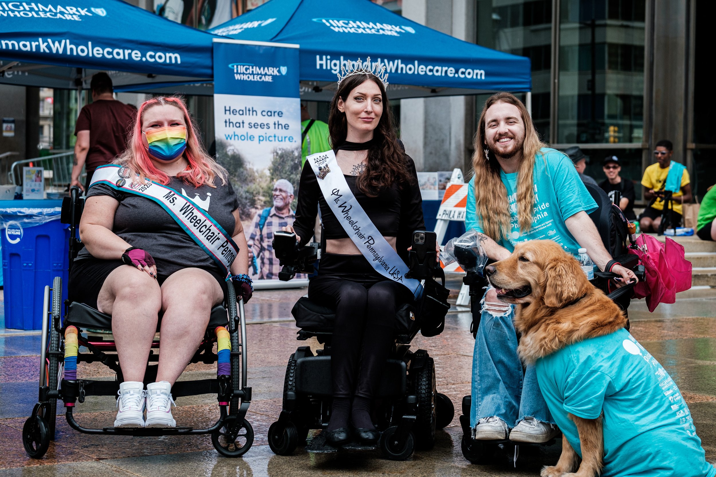 Three wheelchair users  and a service animal pose for a picture in front of the Highmark Wholecare tent in Philly