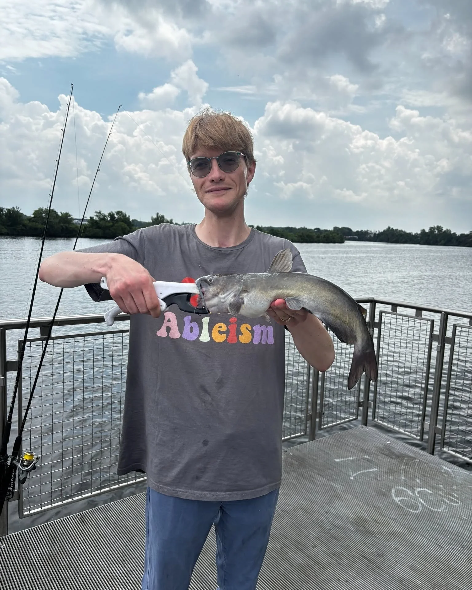 Nico stands on a dock holding up a huge catfish 
