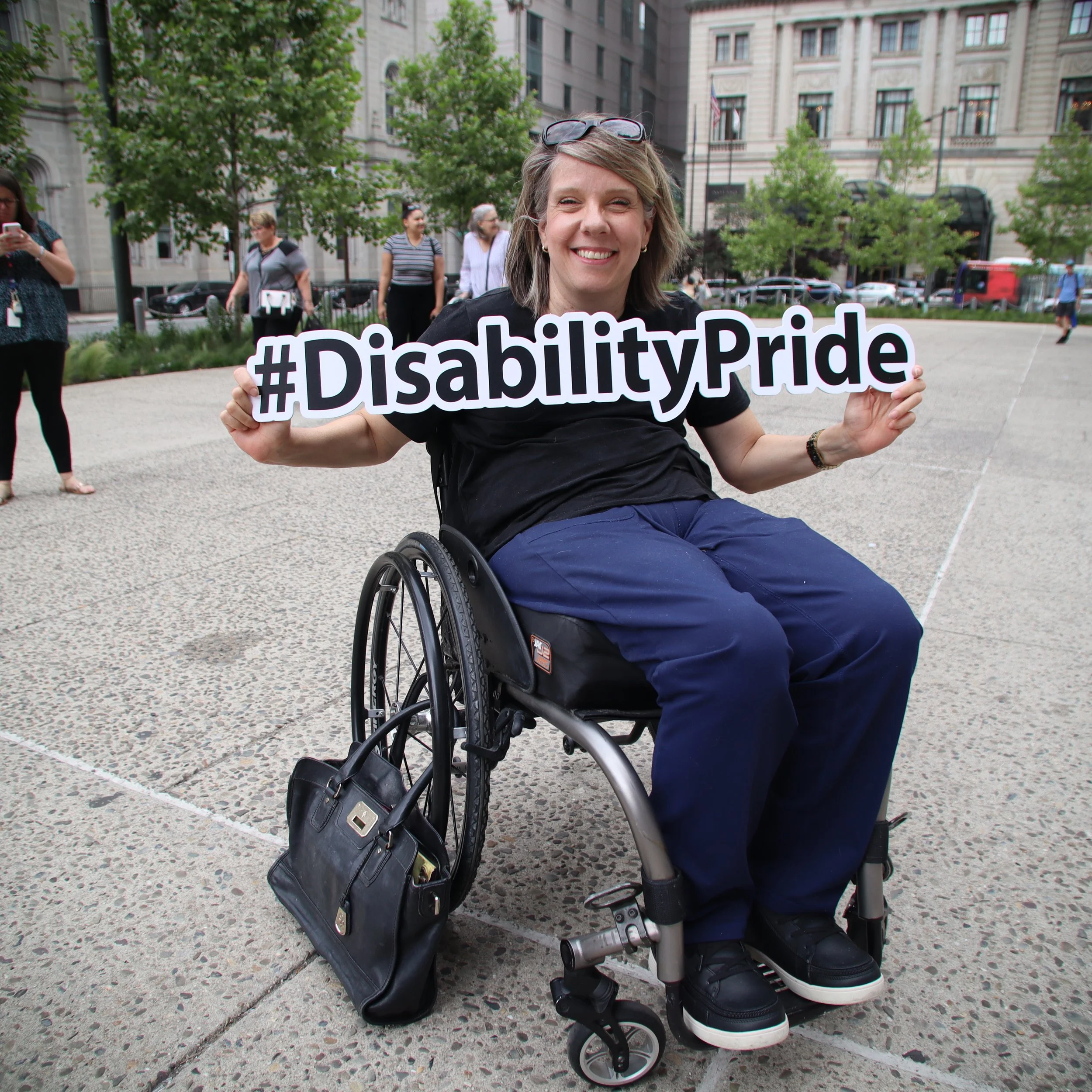 Woman in her wheelchair holding #DisabilityPride sign