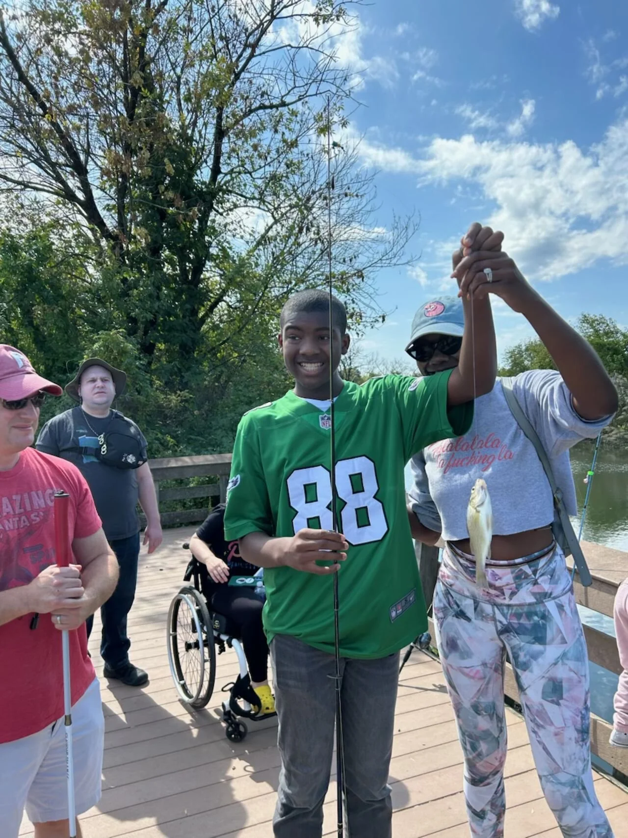 Young man holds up his caught fish with people standing around.