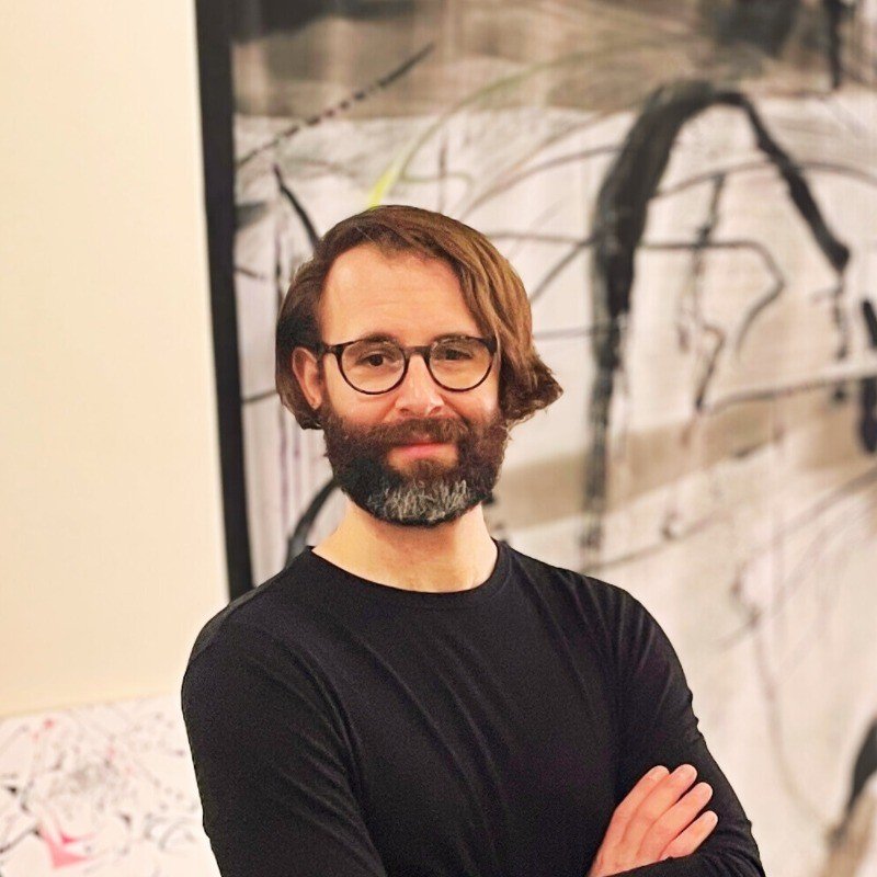 White man with glasses standing in front of an art piece.