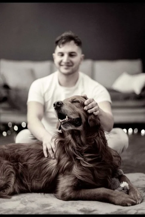 A young man petting a happy, relaxed dog on the head indoors.