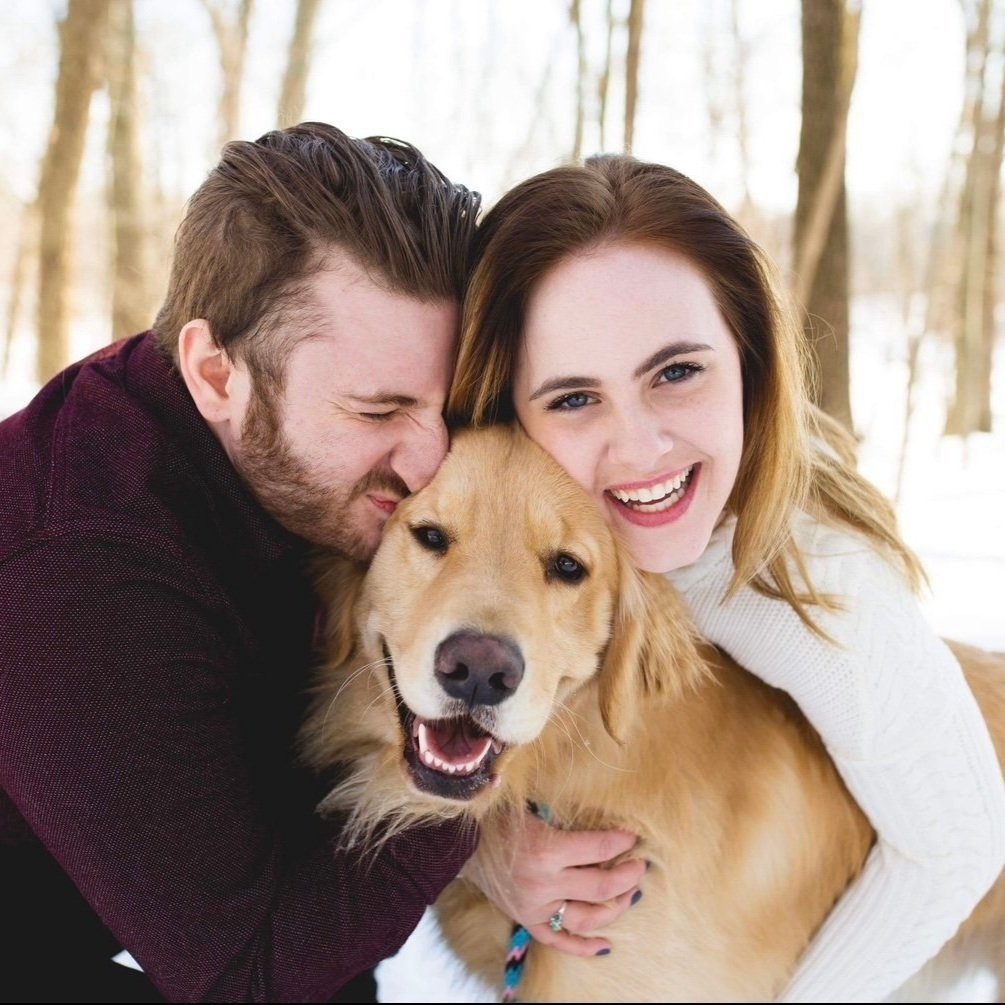 A happy couple and a golden retriever dog outdoors during winter, smiling and cuddling.