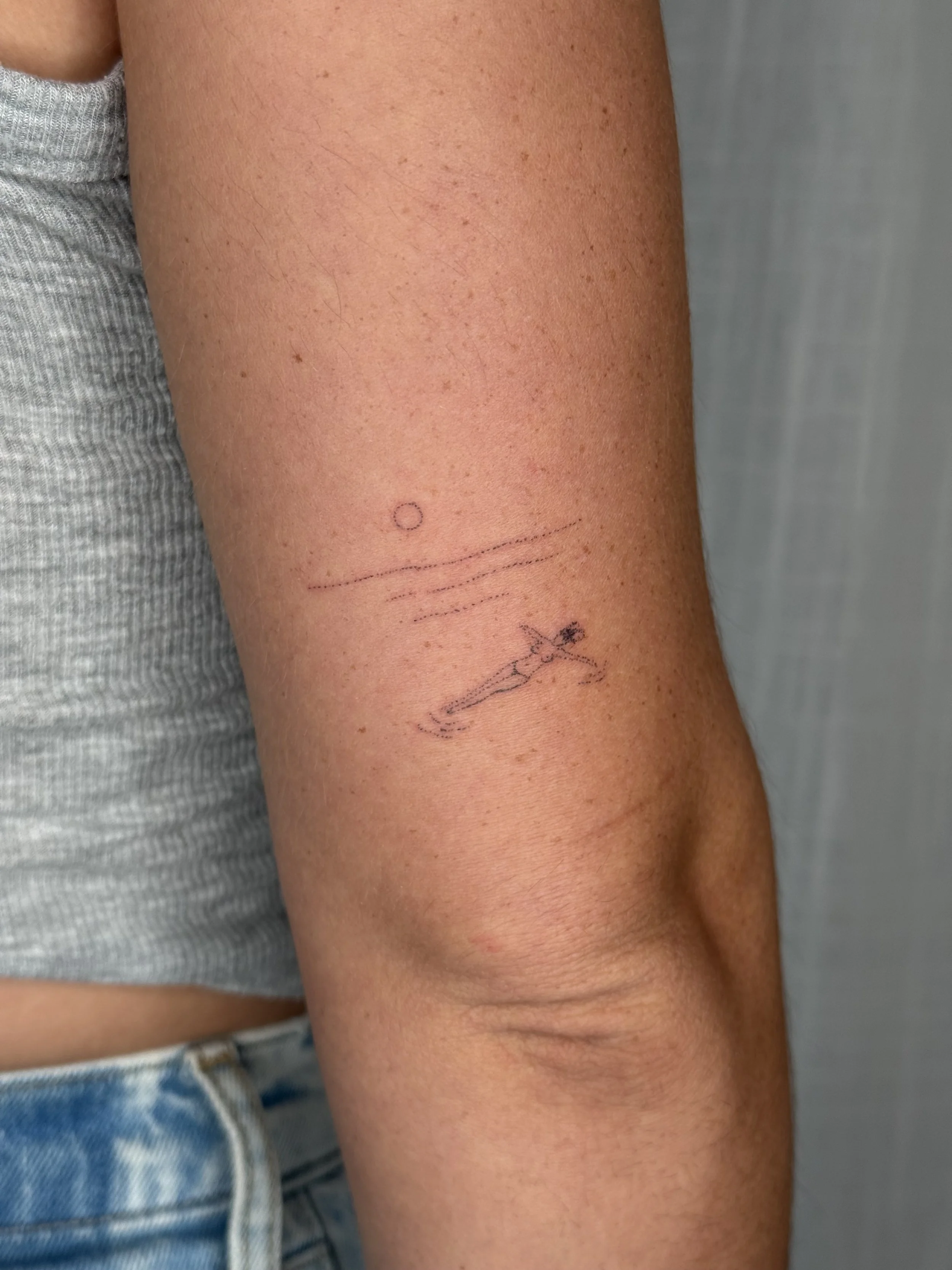 Close-up of a person's upper arm with small freckles and a temporary tattoo of a circle and dots.