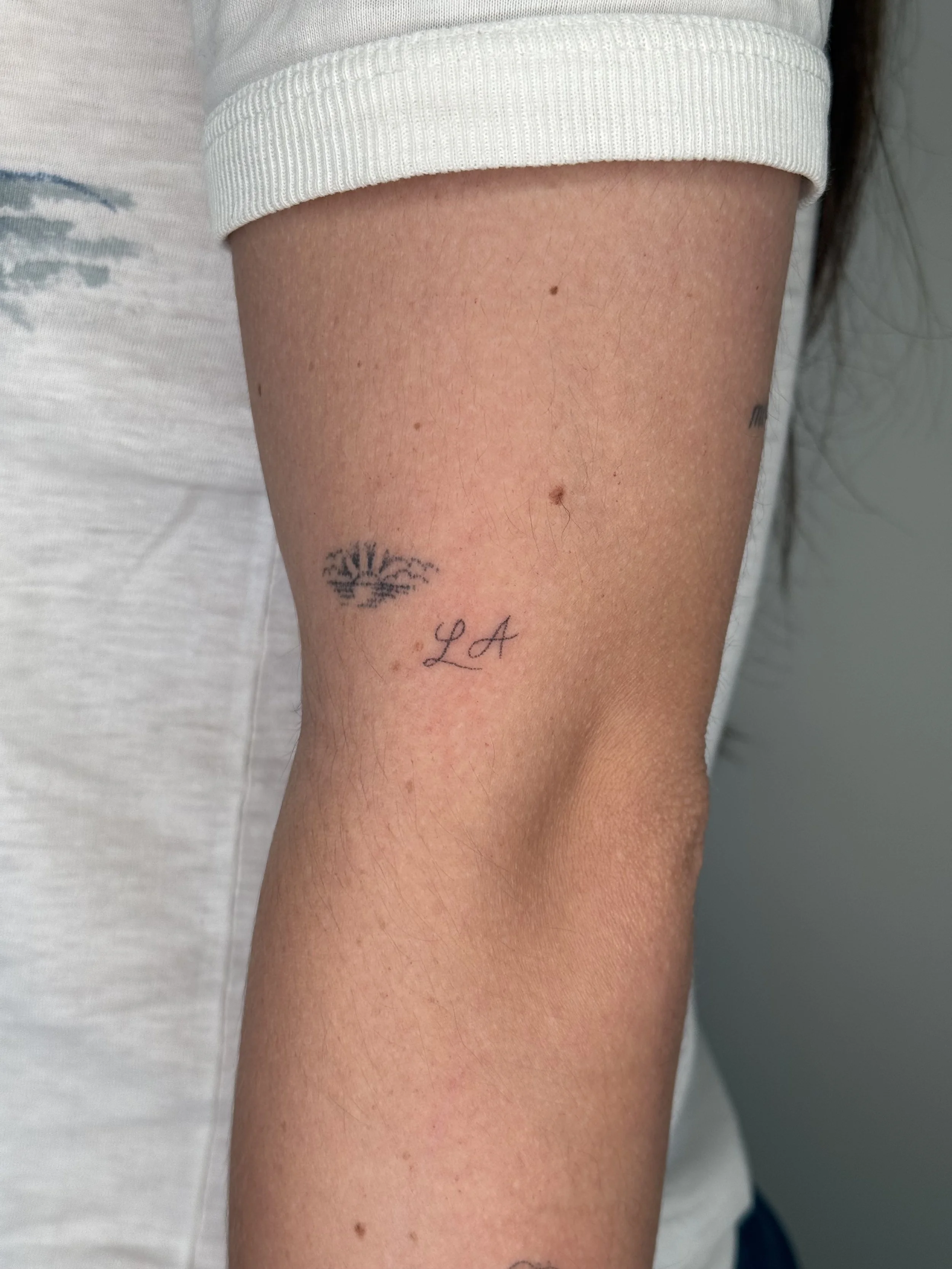 Close-up of a person's arm with a small tattoo of a tree and the initials 'L A' underneath.