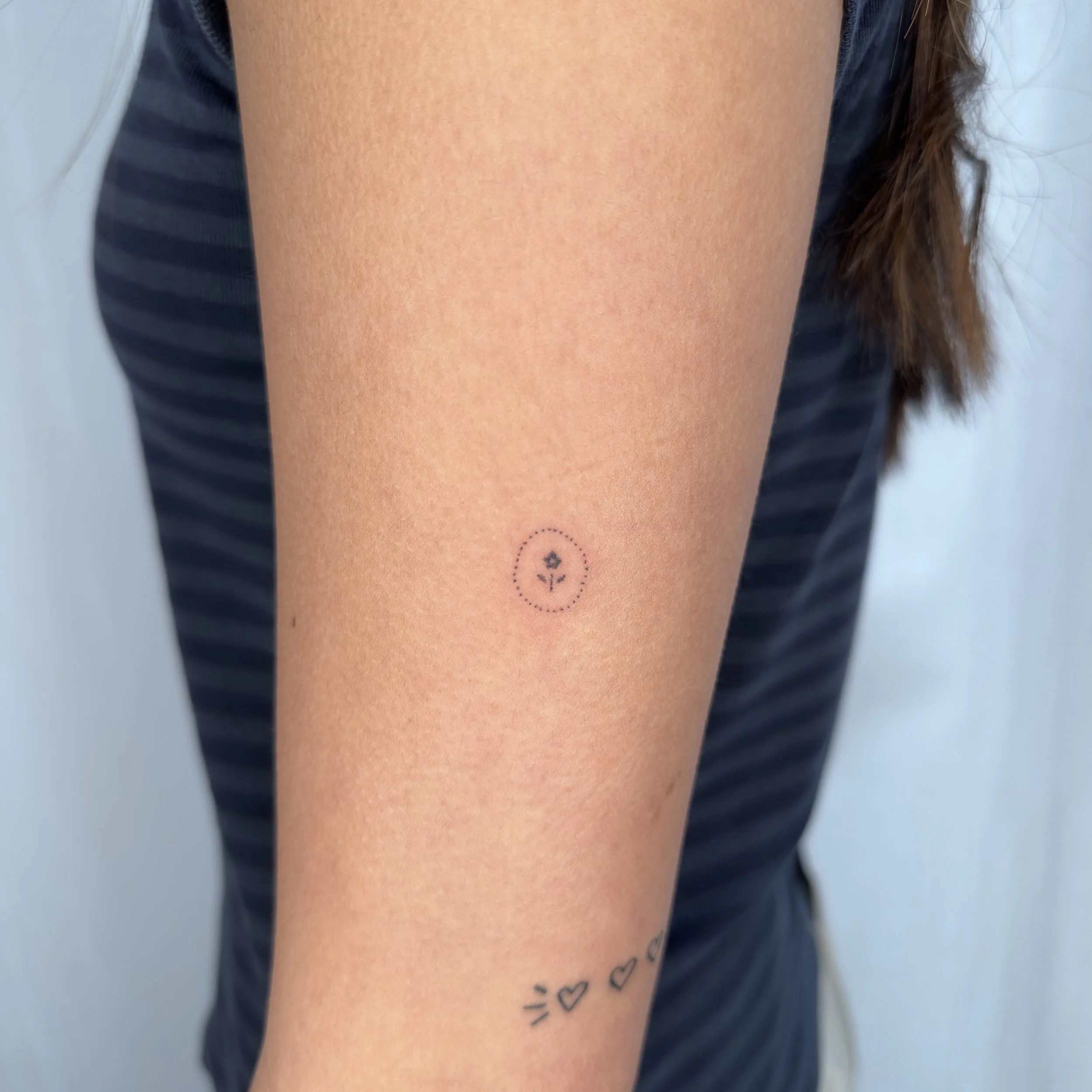 Close-up of a person's forearm with a small tattoo of a floral design inside a dotted circle.