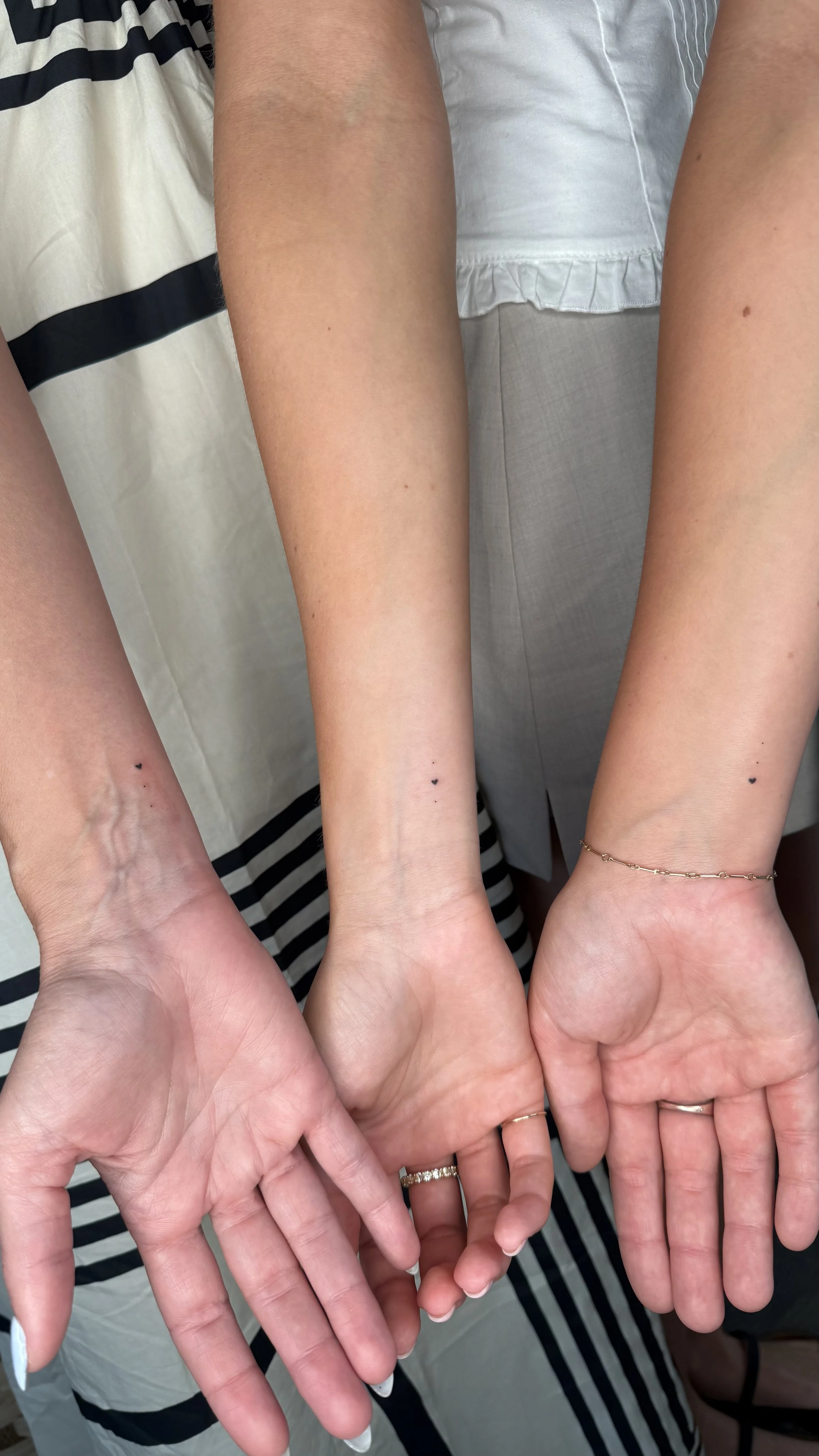 Multiple people are holding out their hands together, displaying rings and tattoos, with a focus on their wrists and hands.