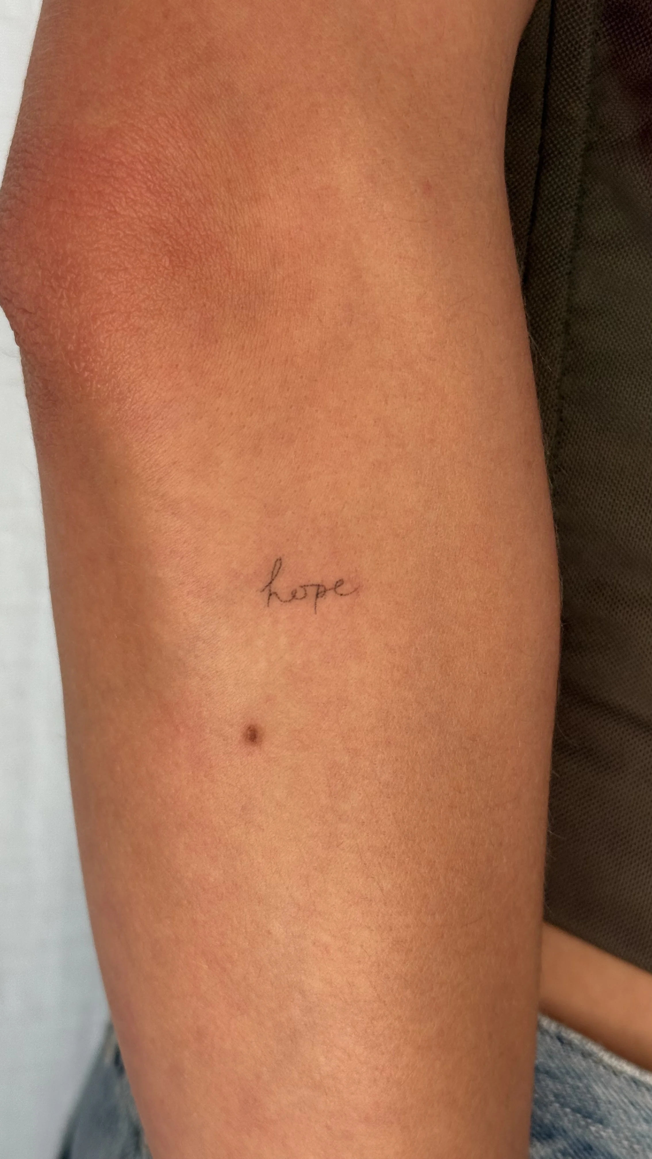 A close-up of a person's upper arm shows a small tattoo with the word 'hope' written in cursive.