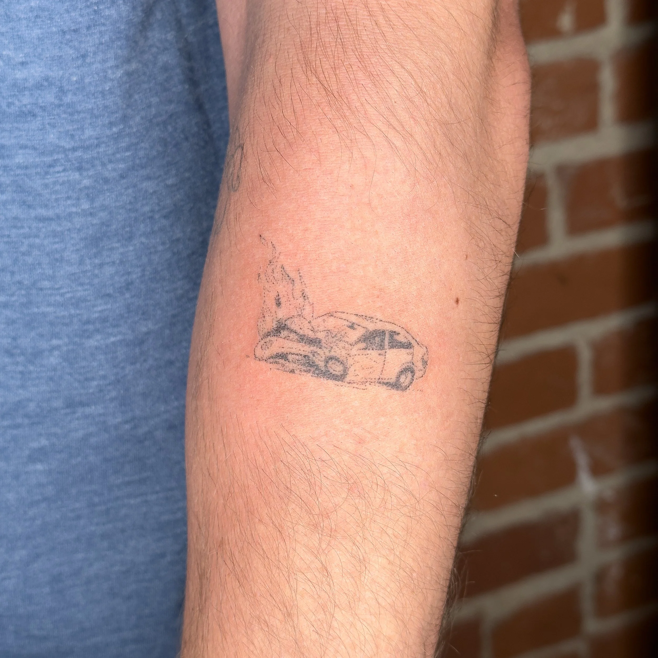 Close-up of a person's forearm with a tattoo of a burning car.