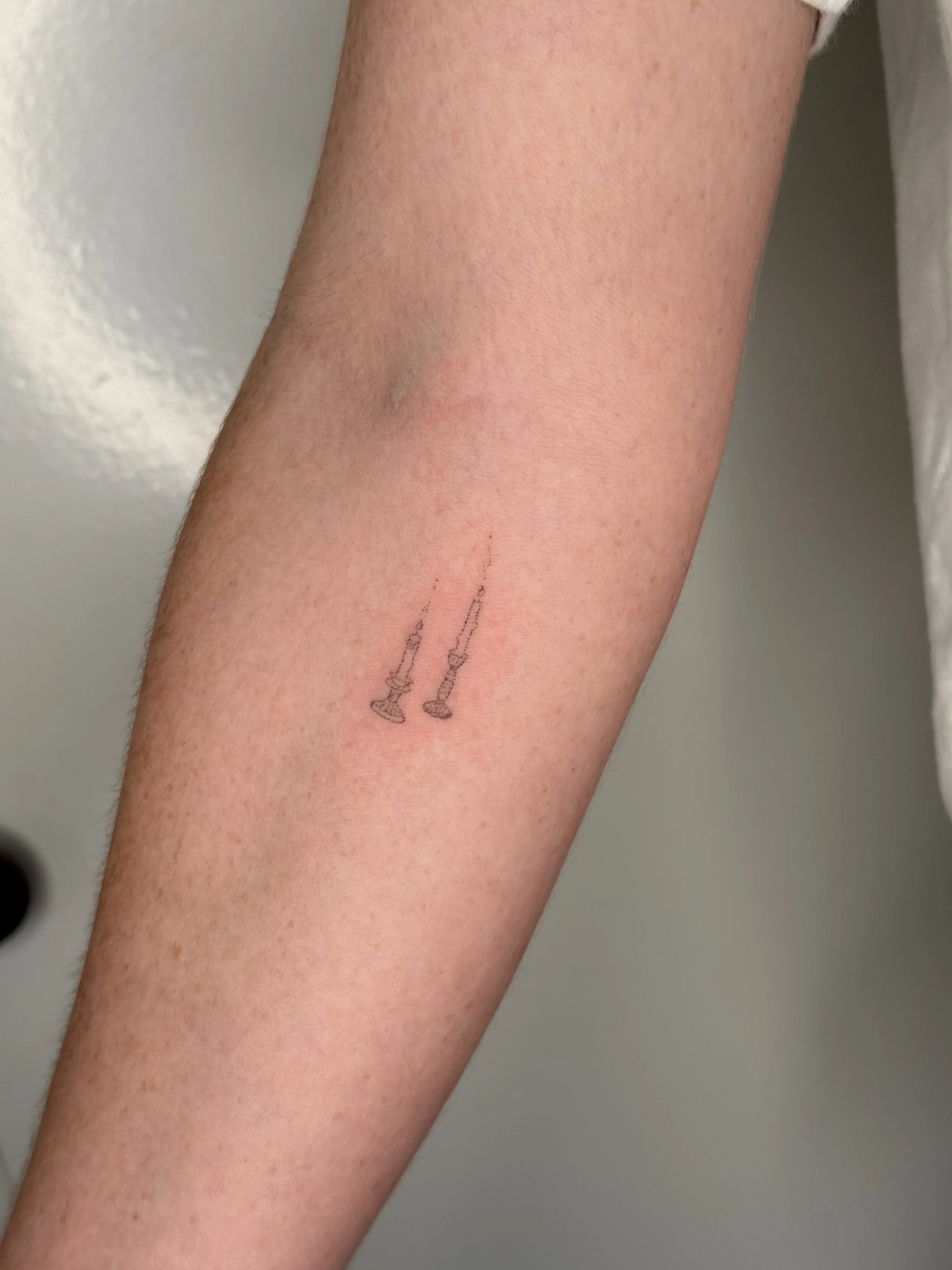 Close-up of a person's forearm with a small tattoo of two chess queens, one slightly larger, near the wrist.