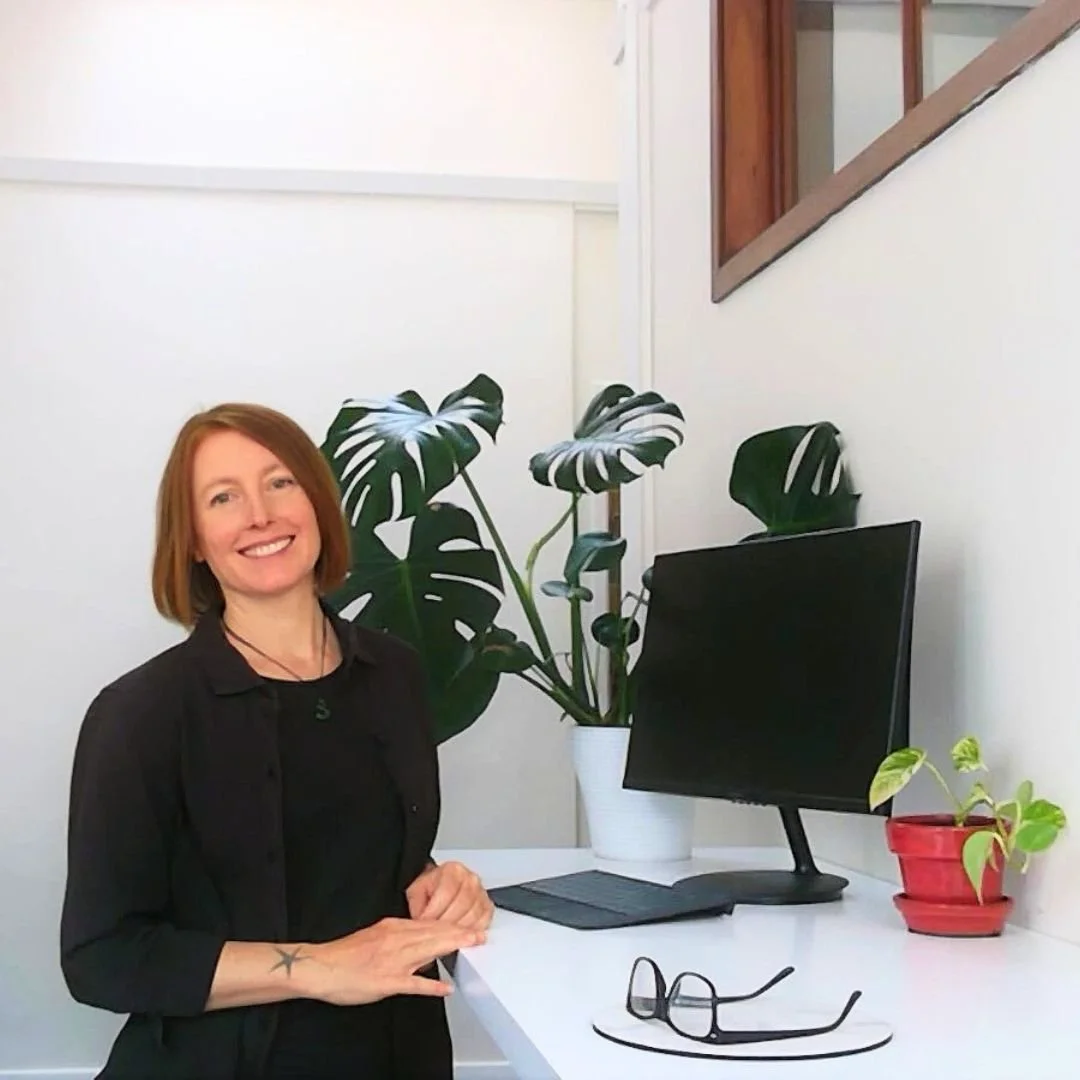 Camille Hoffman at her clinic desk with computer, glasses and monstera fern
