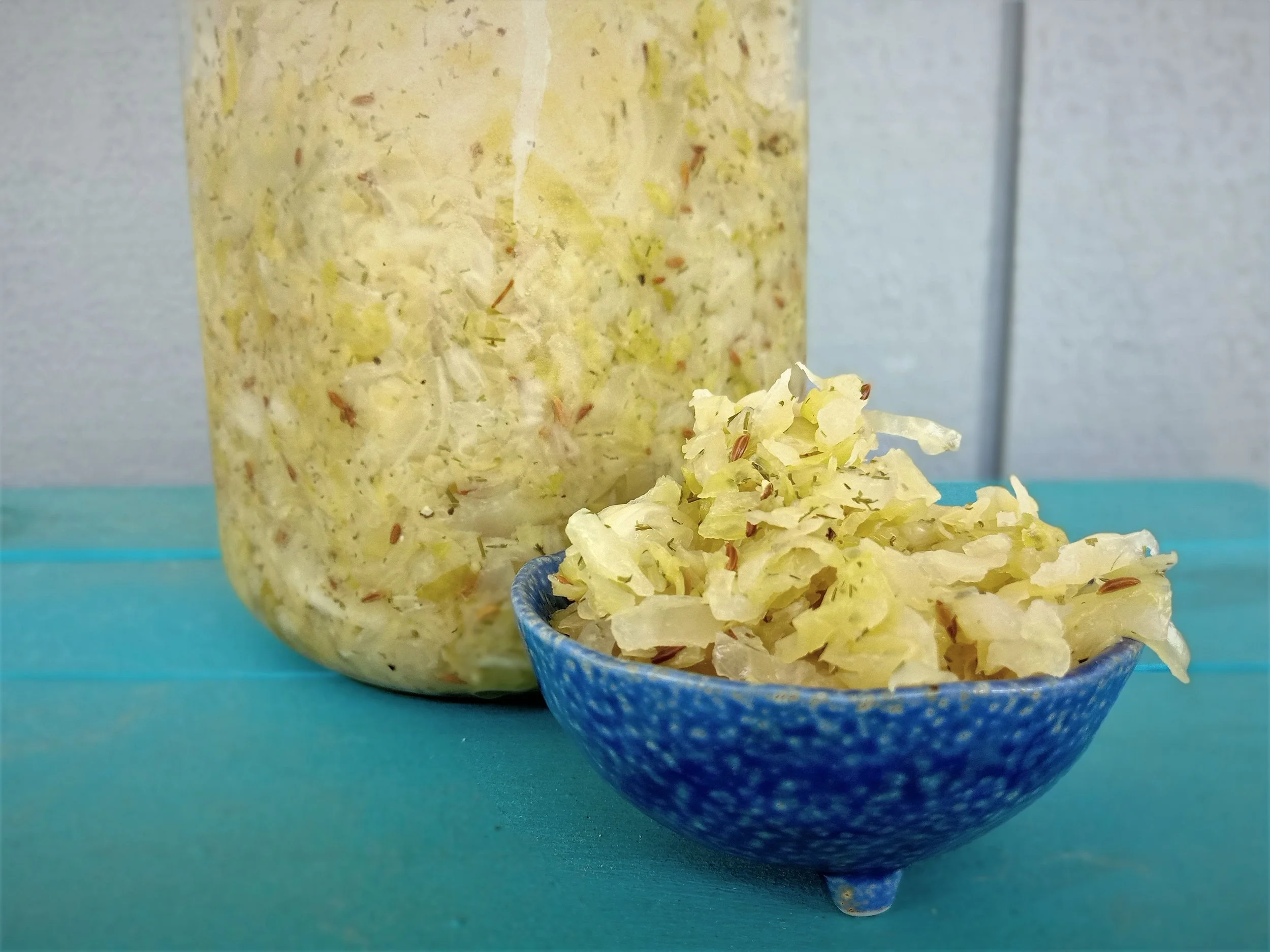 Jar of home-made sauerkraut on blue table, with smaller serving in blue bowl