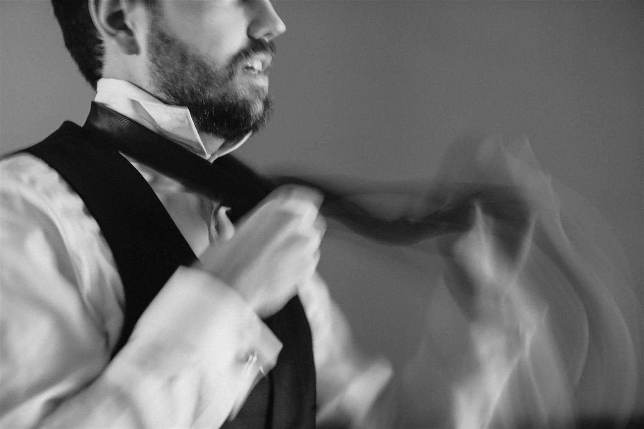 Black and white image of a groom tying his tie.