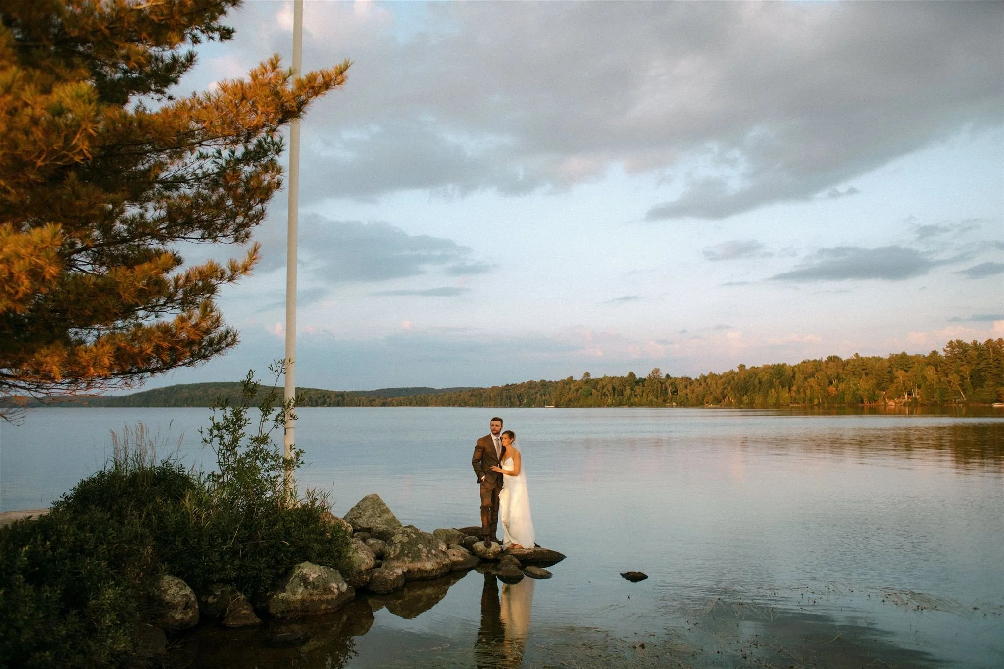 Bride and groom stand together on the rocks overlooking the lake at Northridge Inn wedding at sunset
