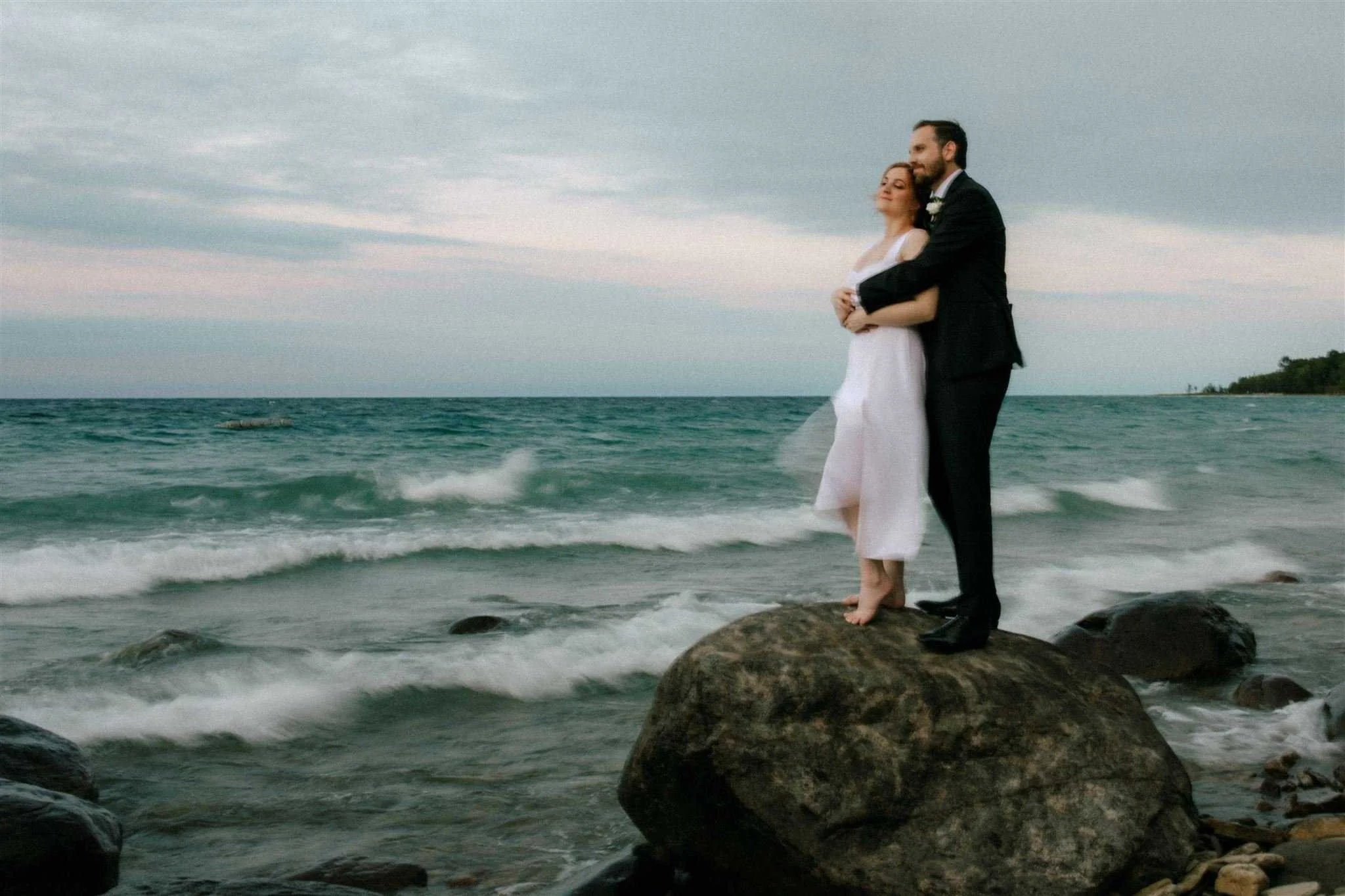 Bride and groom embrace on a rock on the edge of Georgian Bay at Serenity Cottage