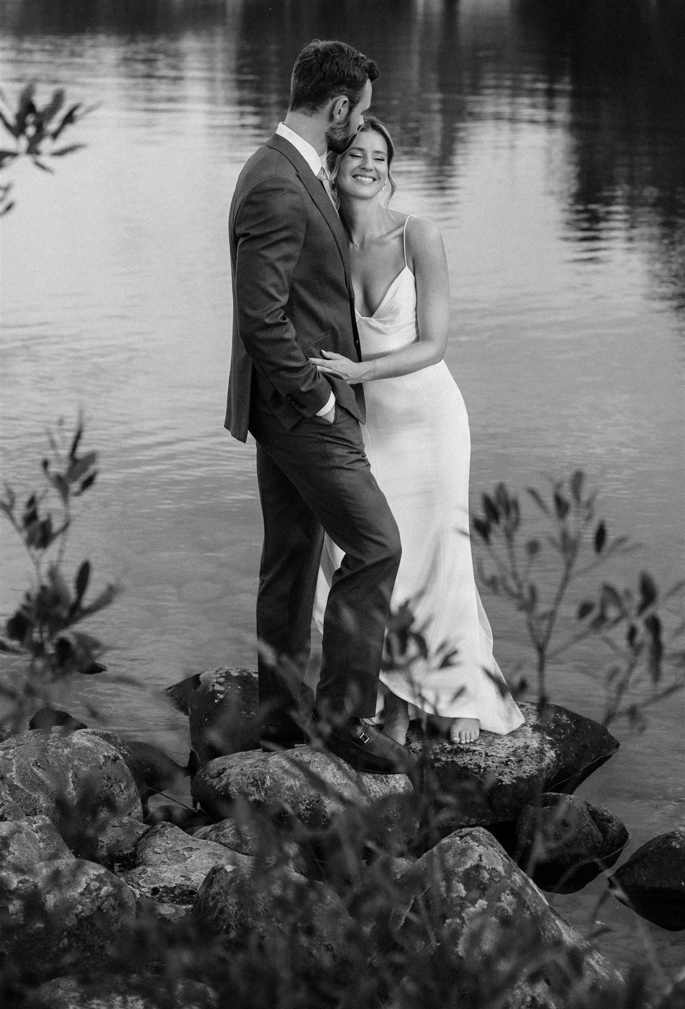 Black and white image of groom kissing bride's temple on lake at Northridge Inn wedding