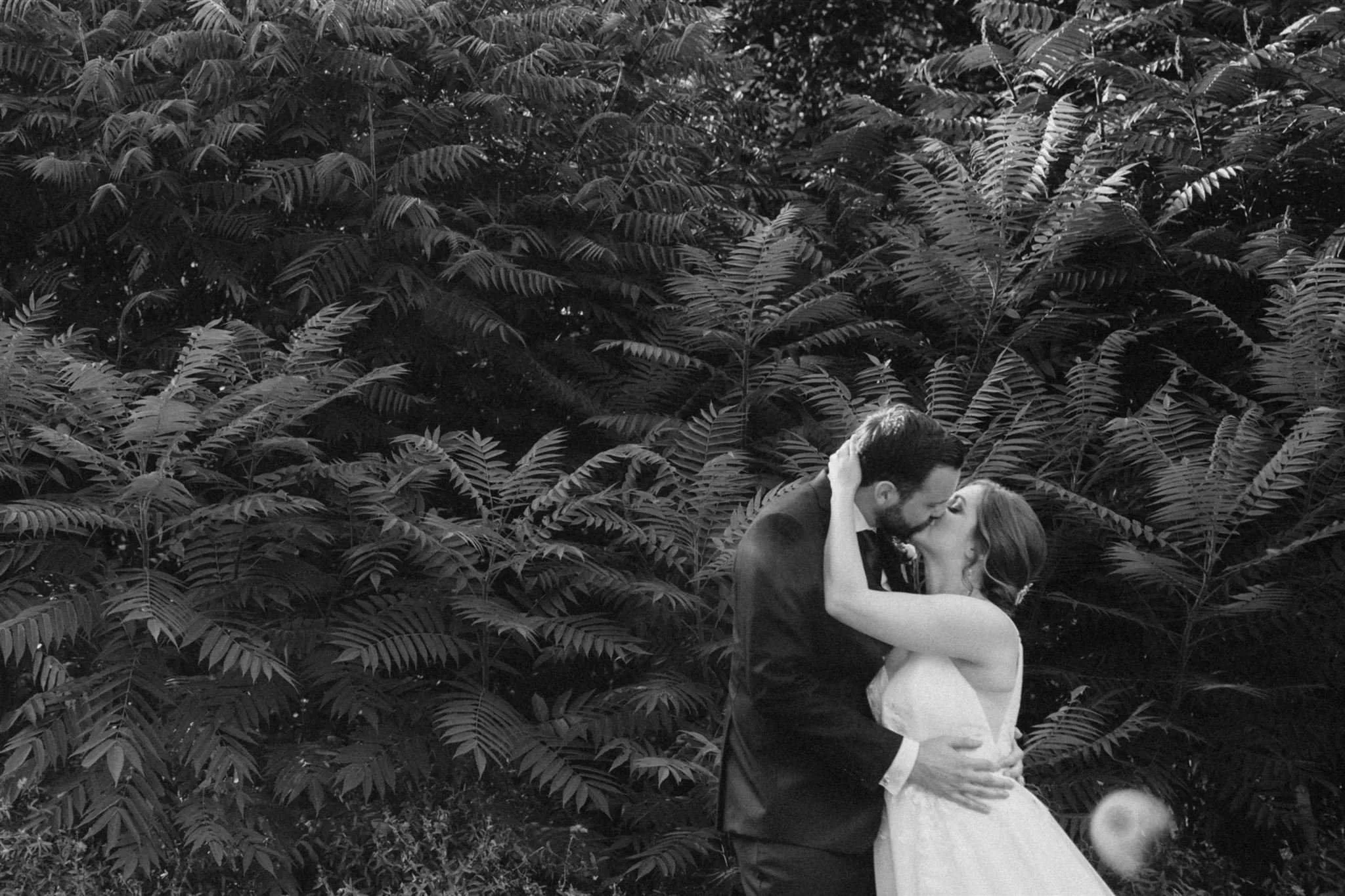 Bride and groom kiss in front of sumac bush in black and white at Owen Sound wedding