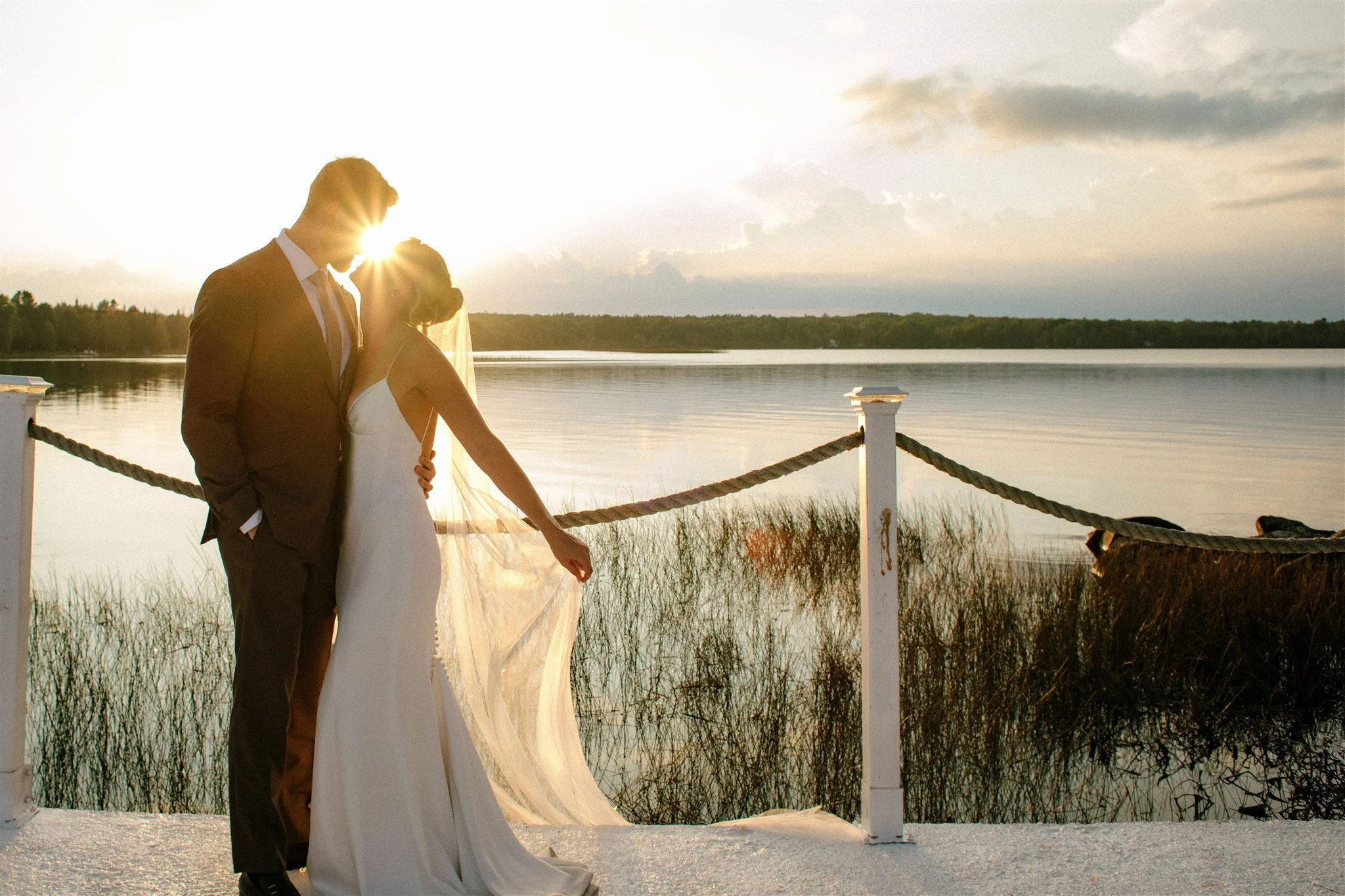 Sun streams in between bride and groom at sunset by the lake at Northridge Inn wedding