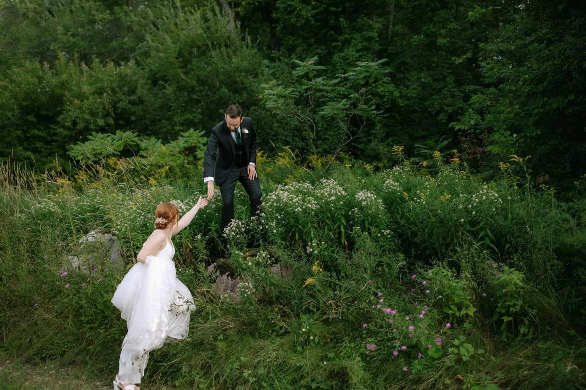 Groom helps bride up into wildflowers at Owen Sound wedding