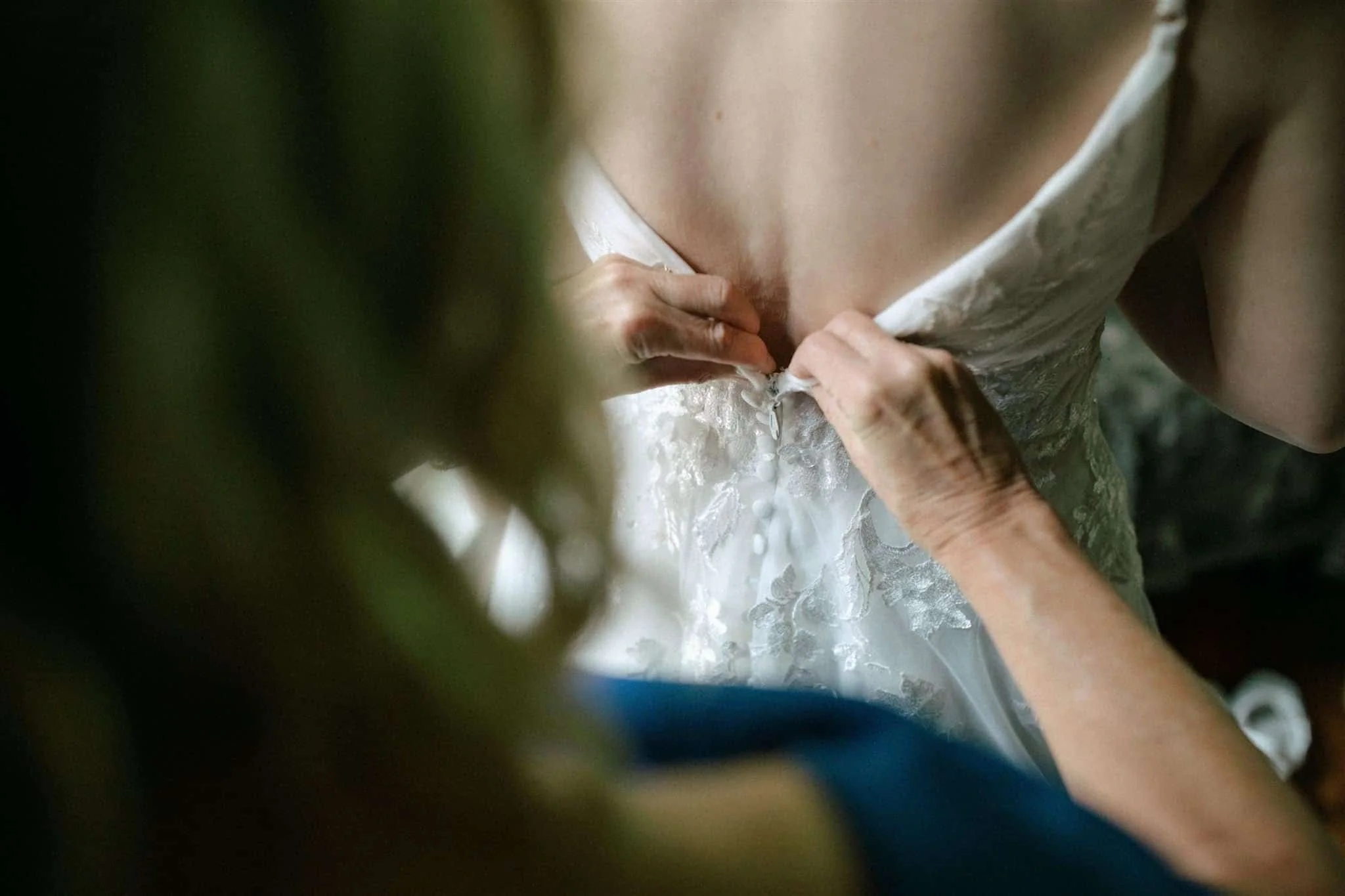 Bride's mother does up her dress by the window of Serenity Cottage.