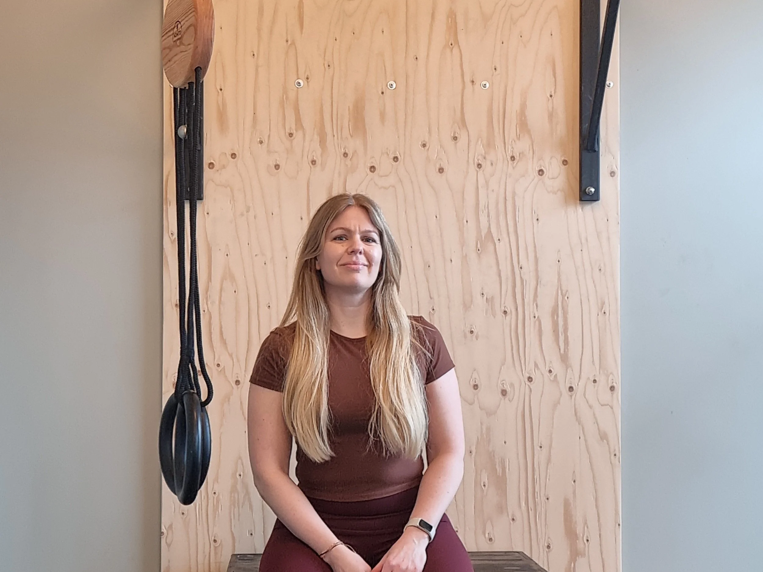 Stina sitter på en bänk på gymmet och ler