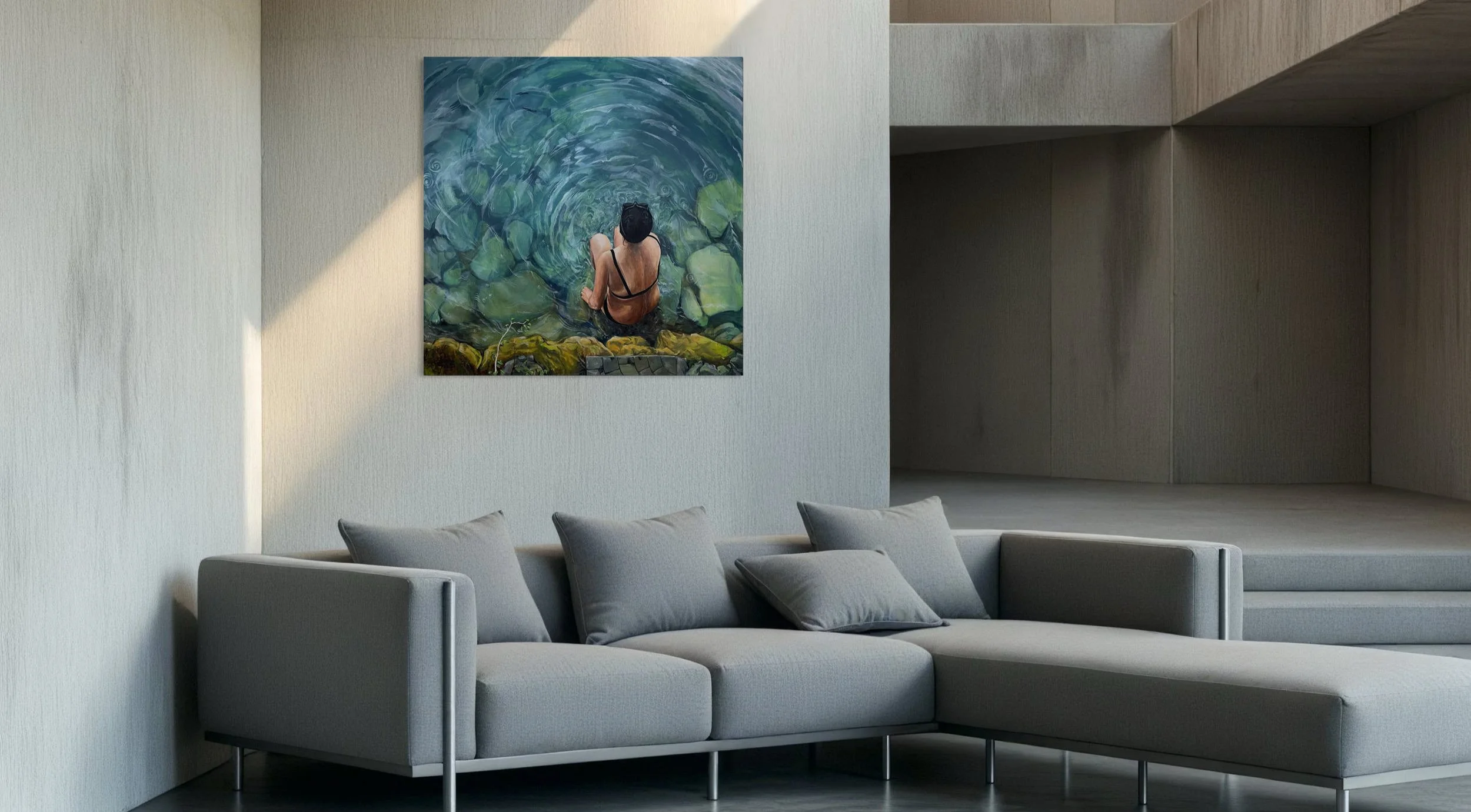 Un salon moderne avec un canapé gris, plusieurs coussins gris et un tableau accroché au mur représentant une personne nageant dans une rivière ou un lac vu de dessus.