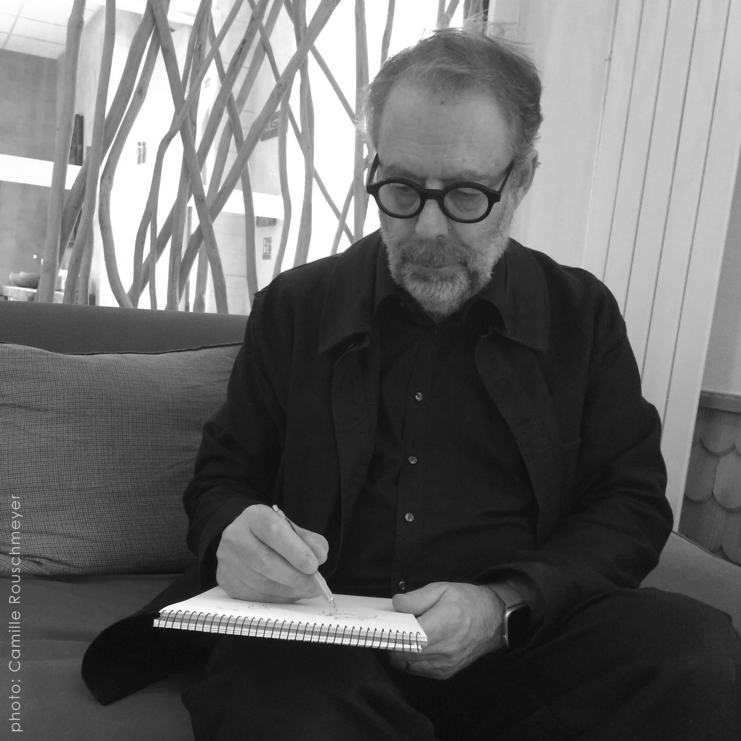 Portrait en noir et blanc de l’artiste peintre figuratif Alain Rouschmeyer dessinant dans un carnet, image illustrant son parcours artistique et sa pratique du dessin d’observation