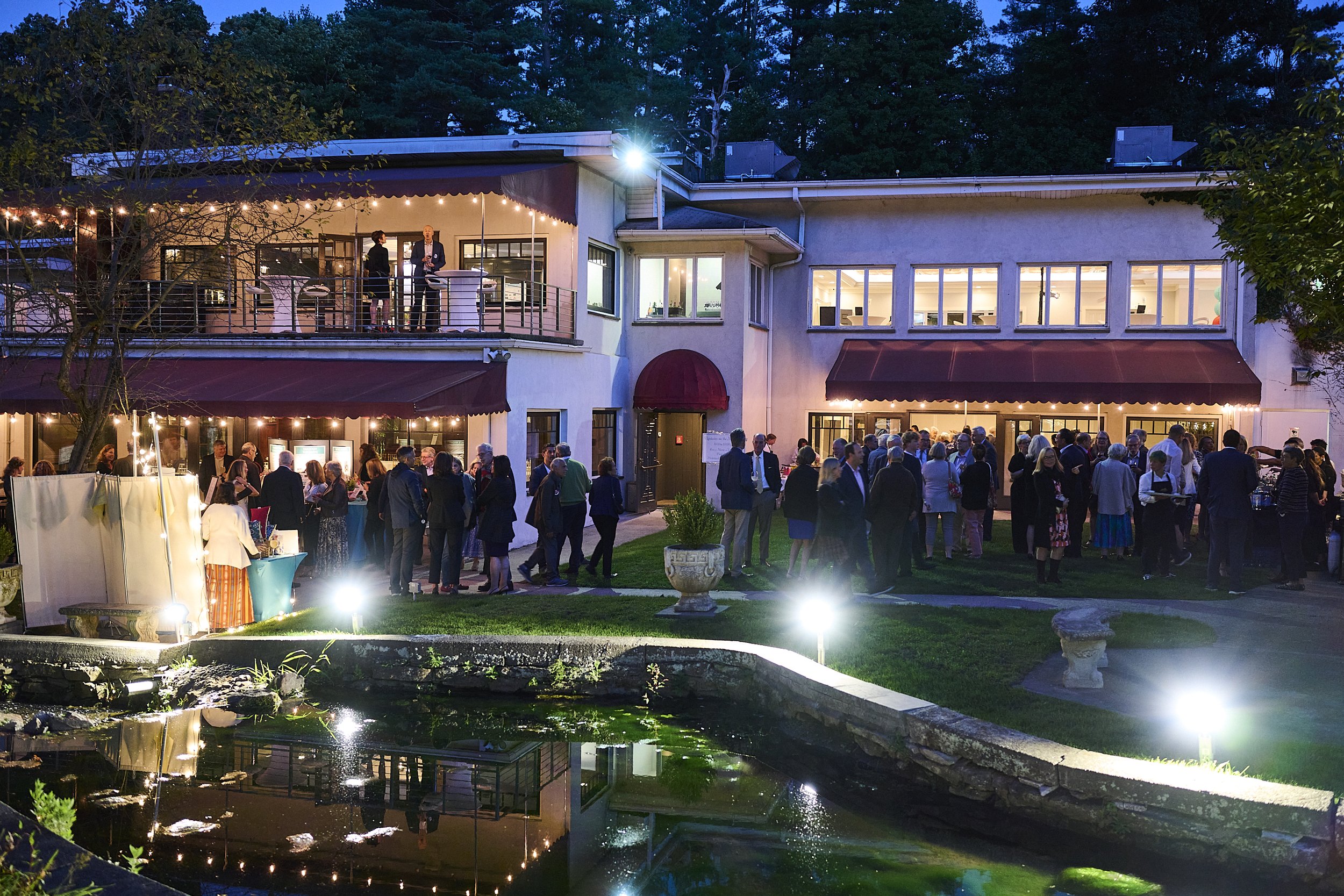 Evening birthday party celebration on the illuminated estate grounds near the water.