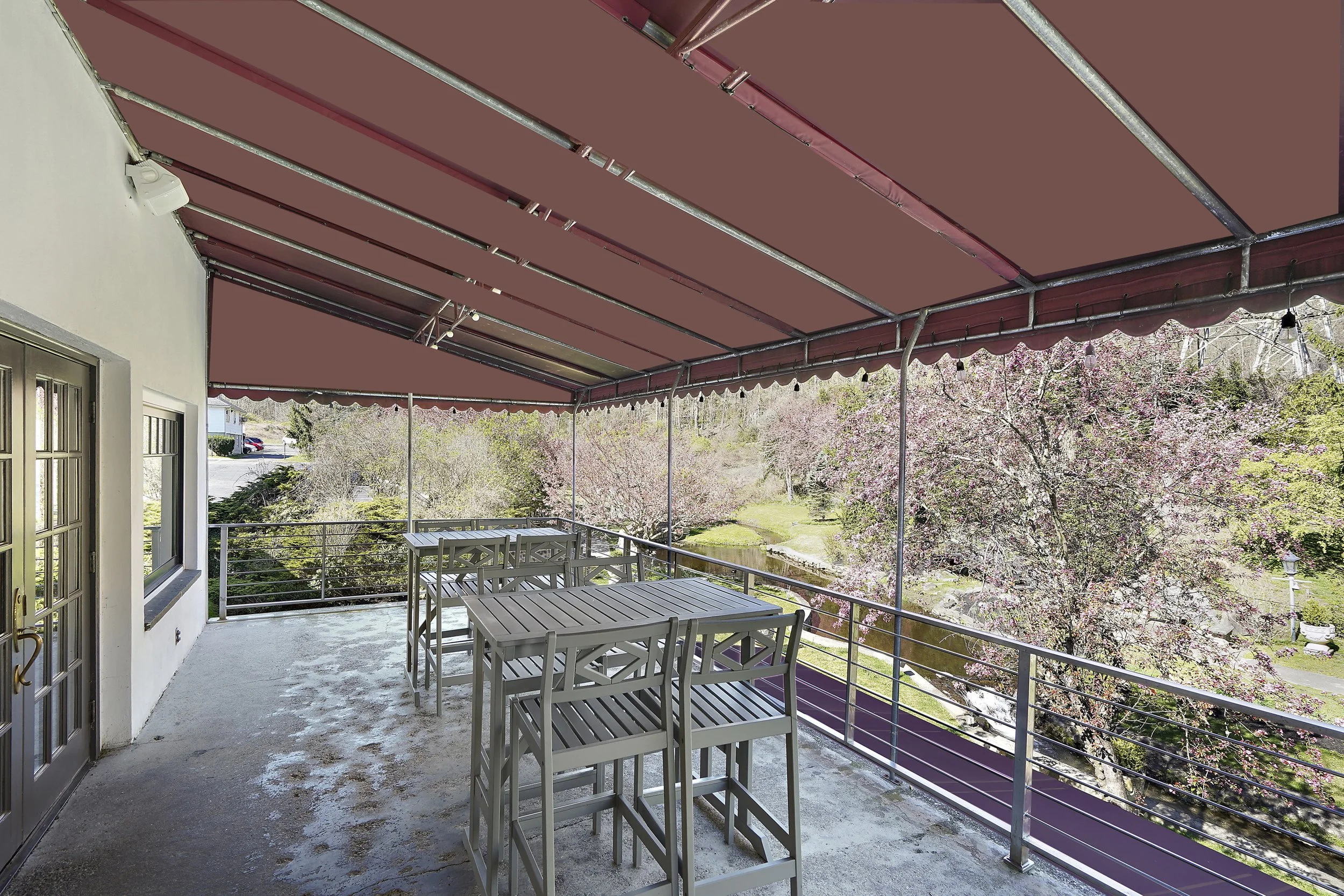 Outdoor balcony with tables and chairs, pink canopy, trees with pink blossoms, and a scenic view of a small pond and park.