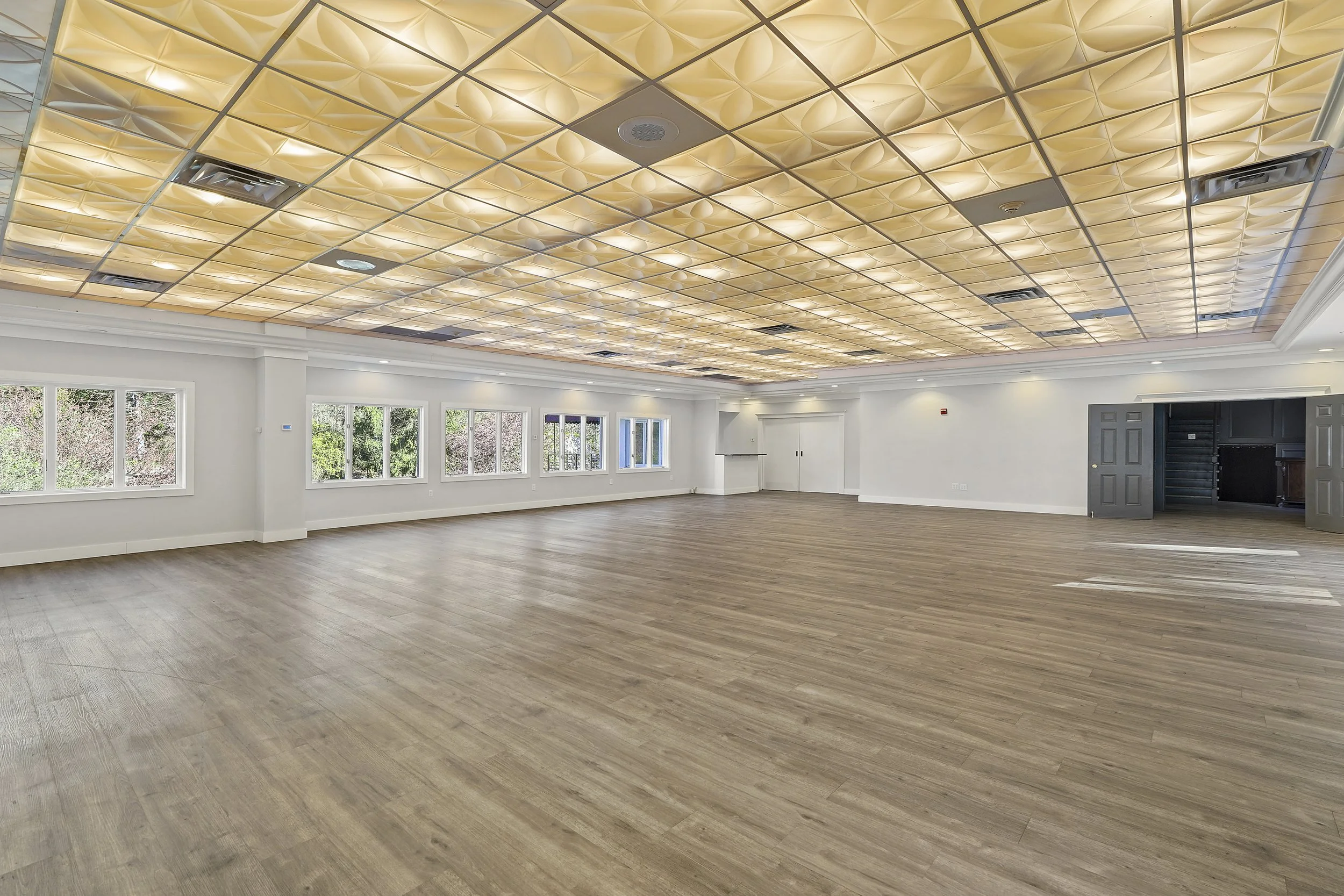 Large, empty banquet hall or event space with a decorative ceiling, several windows, and wooden flooring.