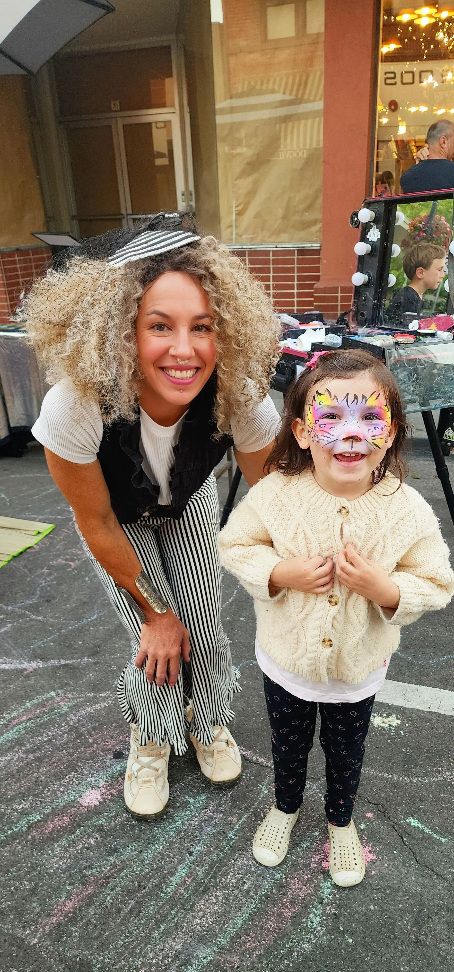 Fun face painter posing with happy child with rainbow cheetah facepaint