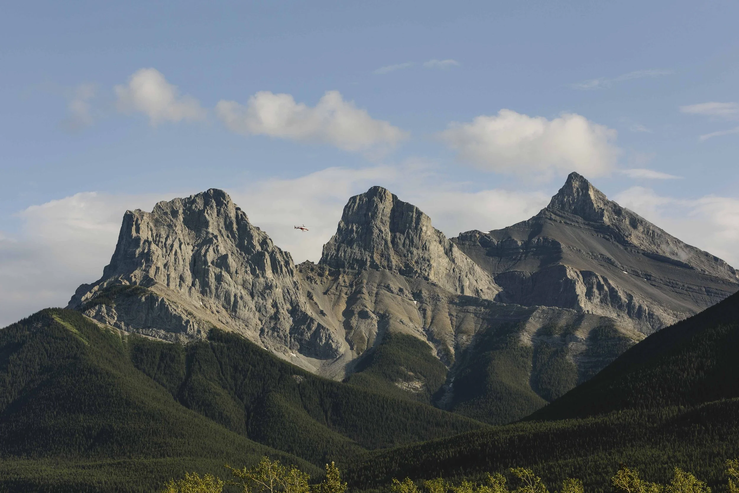 20230704, Three Sister Mountains, Canmore - A helicopter flies along side the Three Sisters Mountains