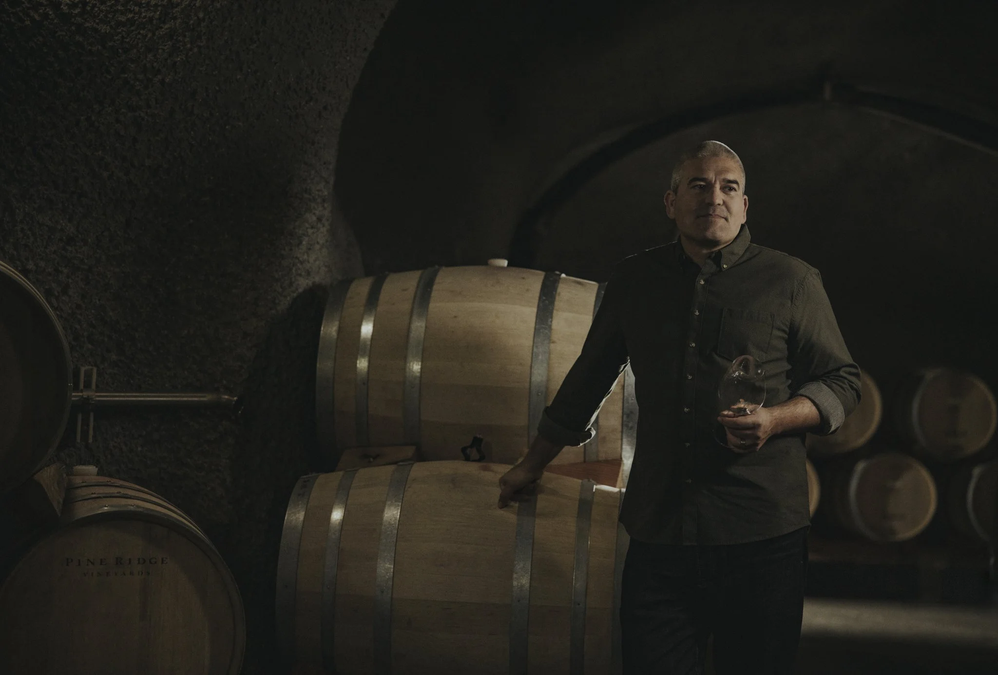 A winemaker standing among barrels in a wine cellar.