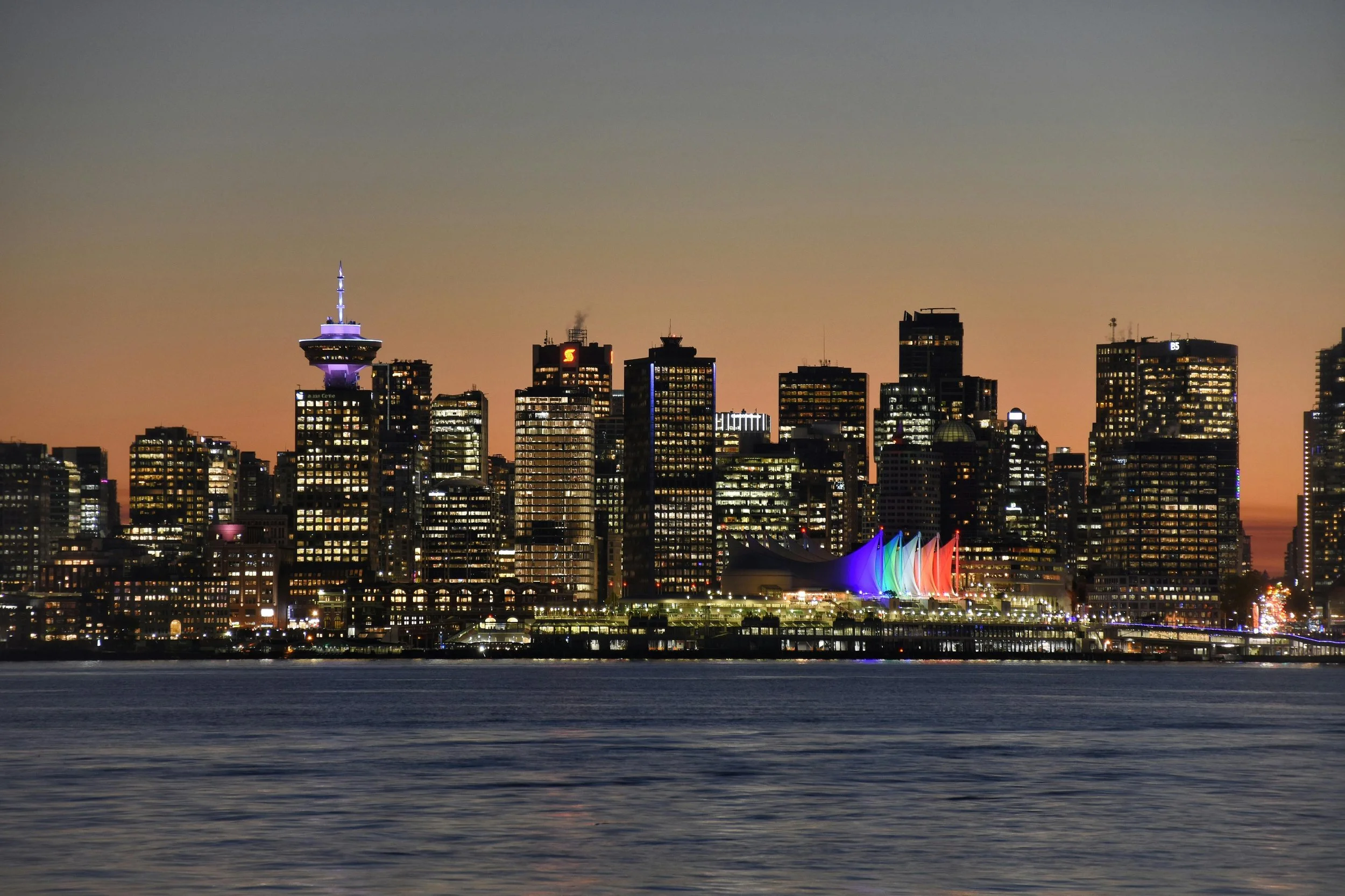 Night view of Vancouver skyline with illuminated buildings and colorful sail-shaped structures along the waterfront.
