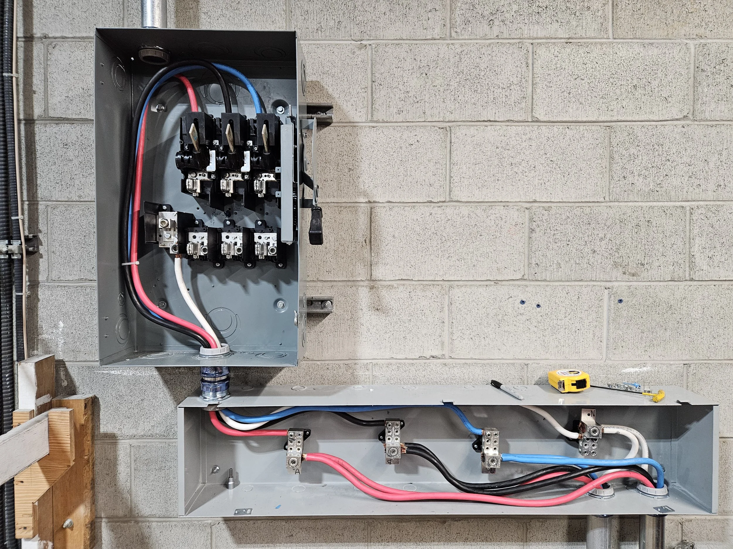 Electrical wiring in metal conduit boxes with tools on a cinder block wall.