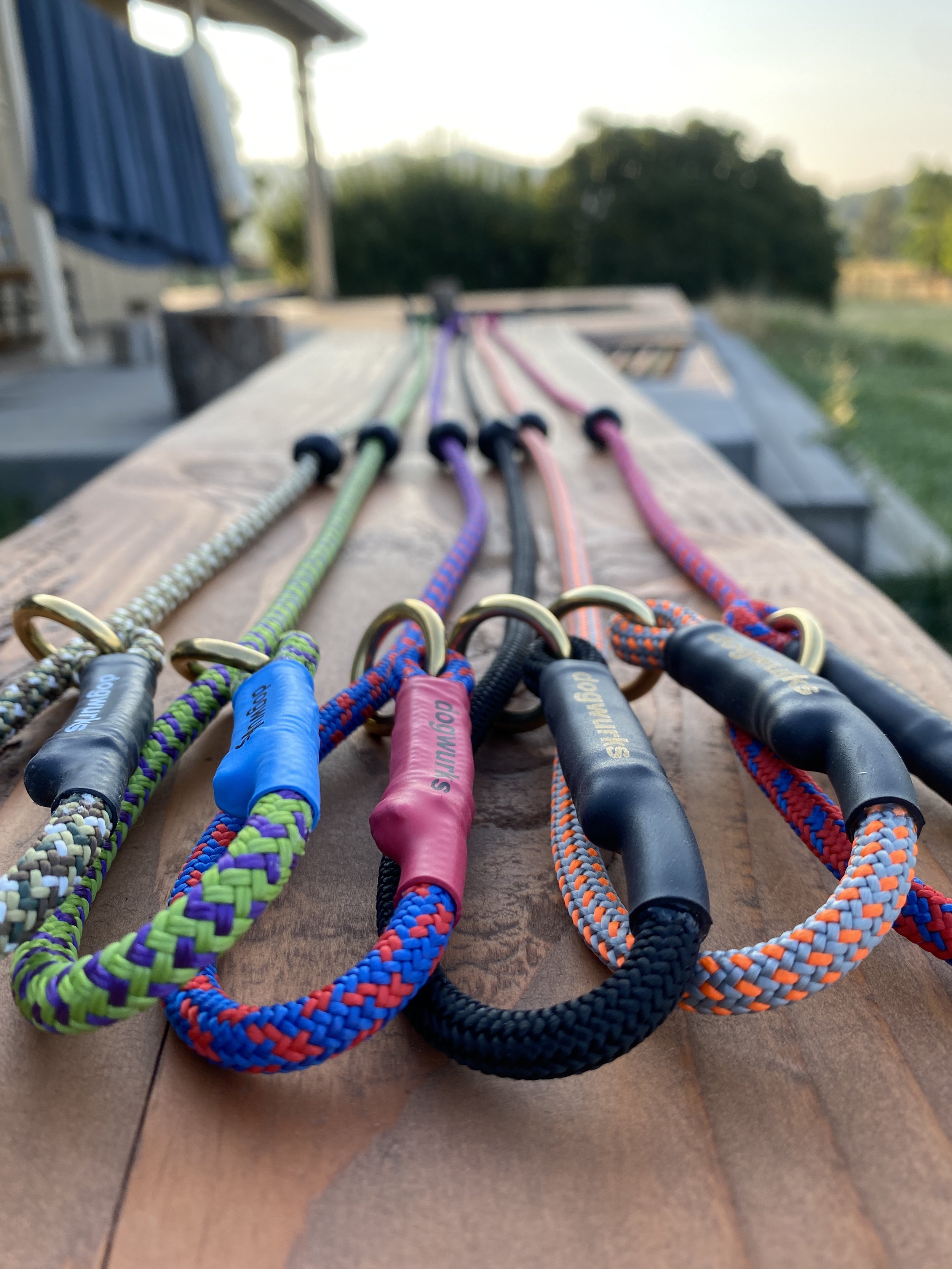 Multiple climbing ropes with different colors and patterns laid out on a wooden surface outdoors, with a blurred background of trees and sky.